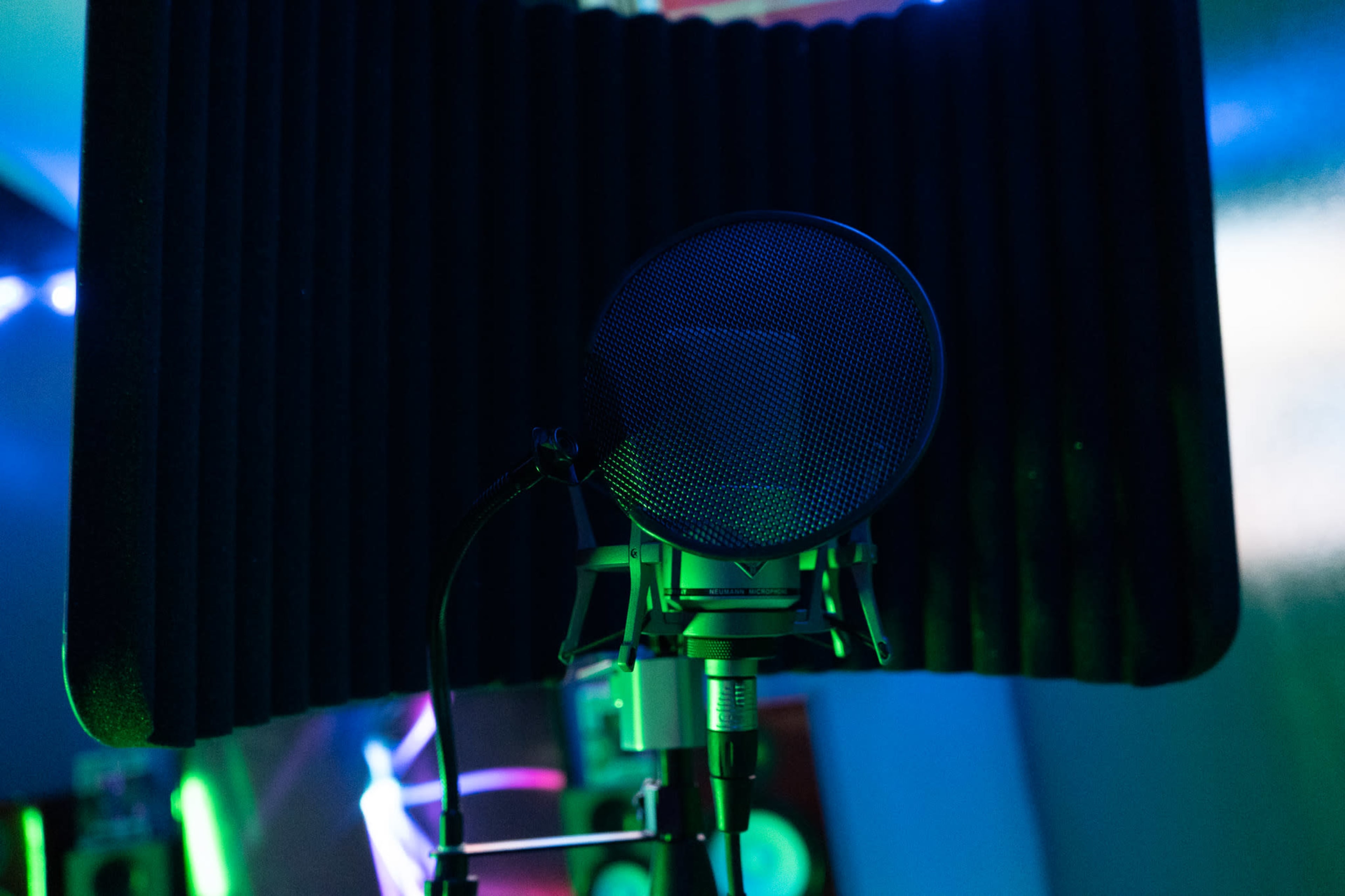 A microphone is positioned in front of a soundproof foam panel in a dimly lit recording studio.