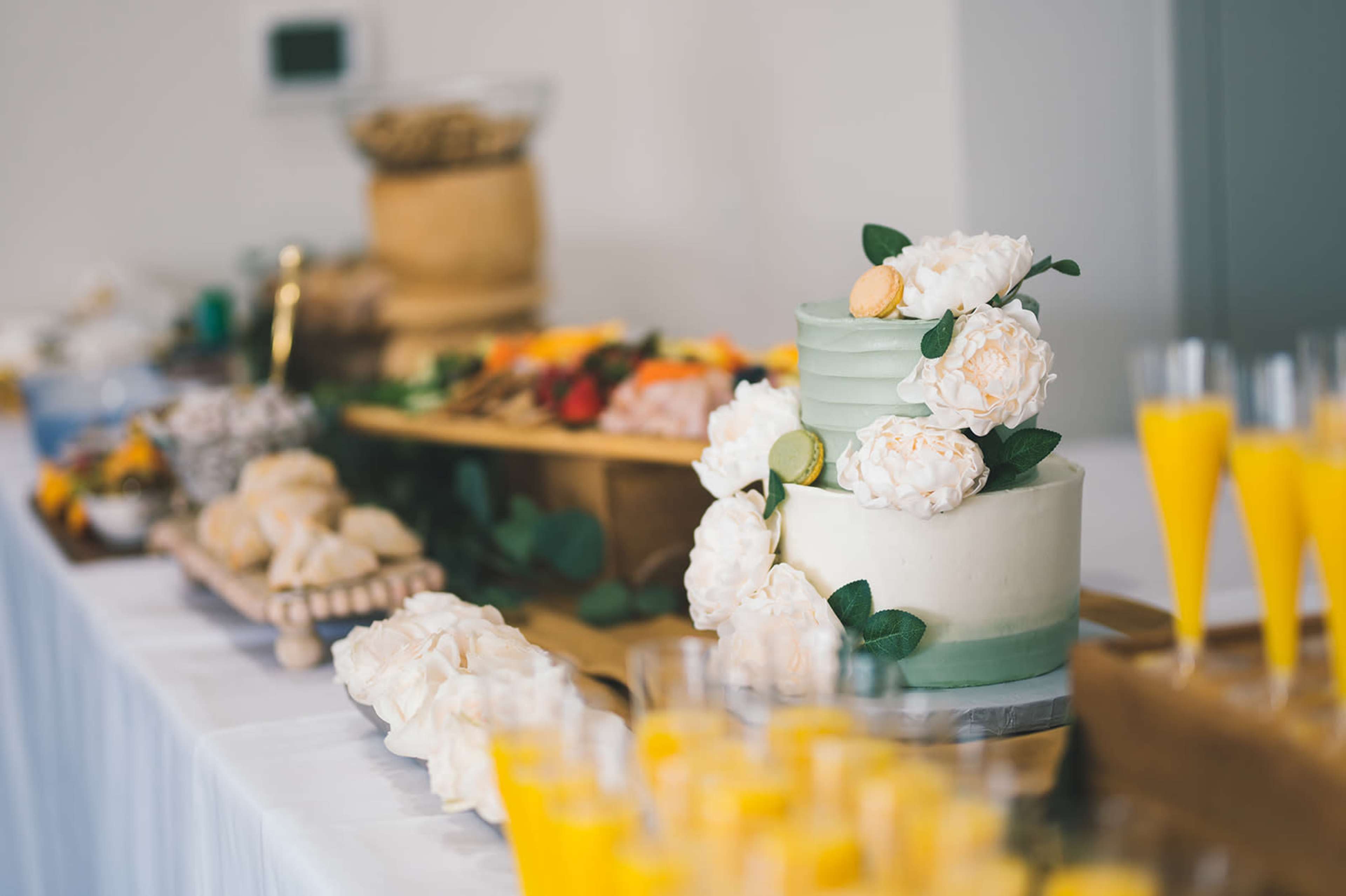 A neatly arranged dessert table features a tiered cake adorned with white flowers, alongside an assortment of pastries and fruit.