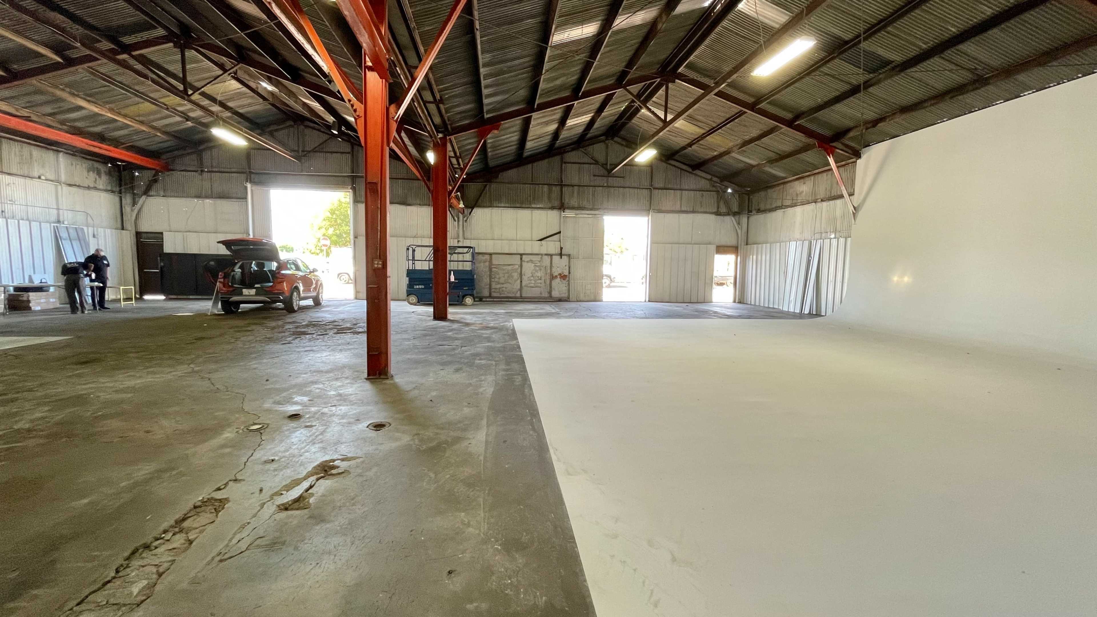An empty warehouse interior with red metal beams, a concrete floor, and two open doors leading outside.