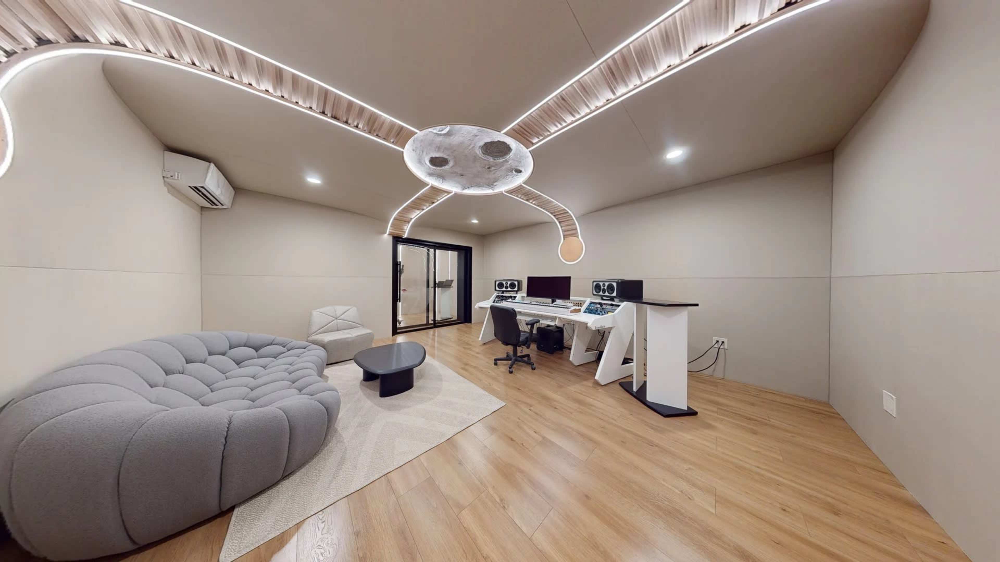 A modern room featuring a curved gray sofa, a small black table, and two computer workstations with a unique ceiling design.