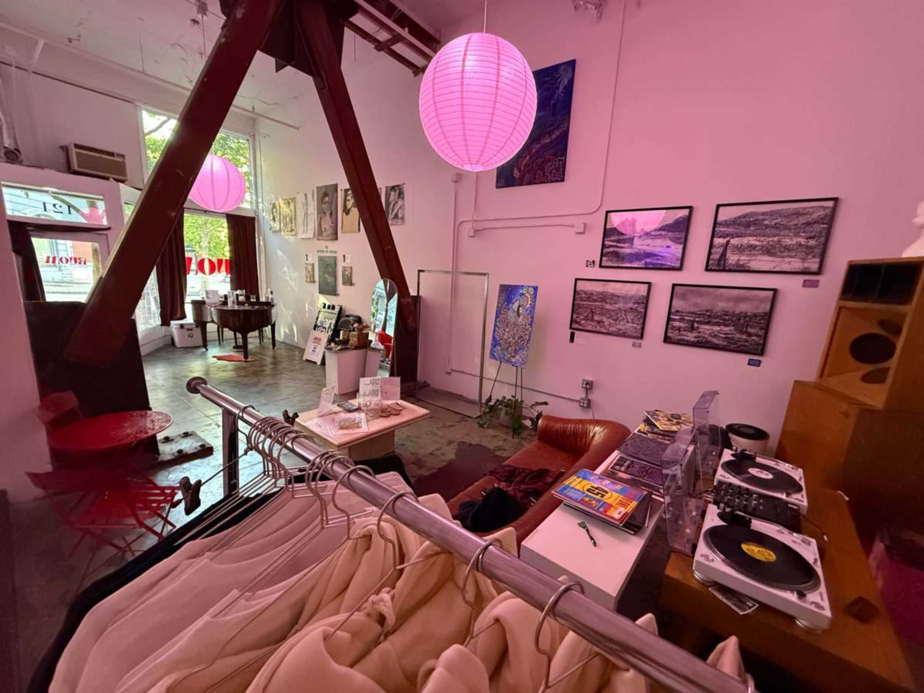 The image shows a colorful art gallery and shop featuring various artworks on the walls, a record player, and seating areas.