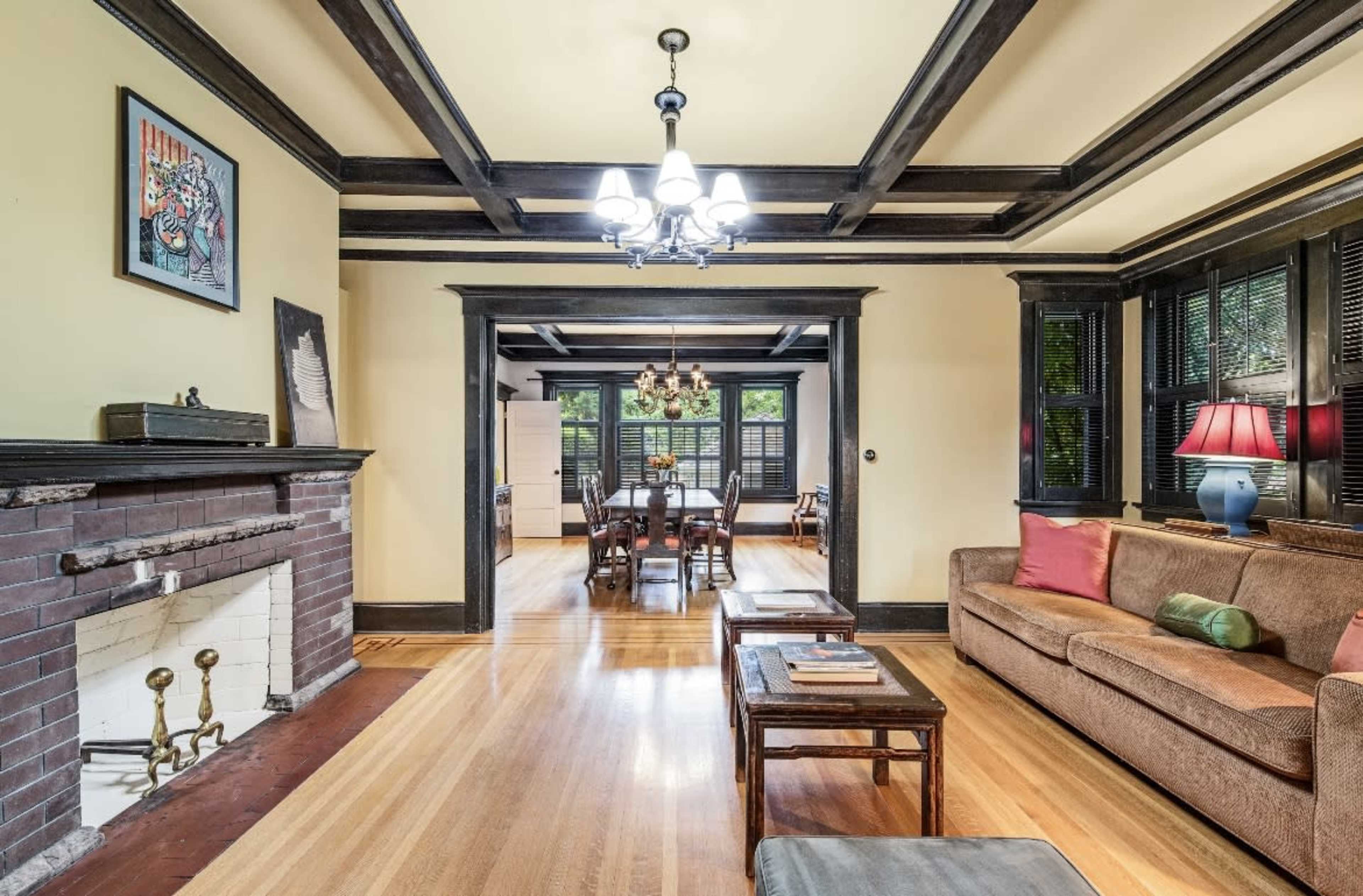 A living room features a brown sofa, a coffee table, and a fireplace, with a dining area visible in the background.