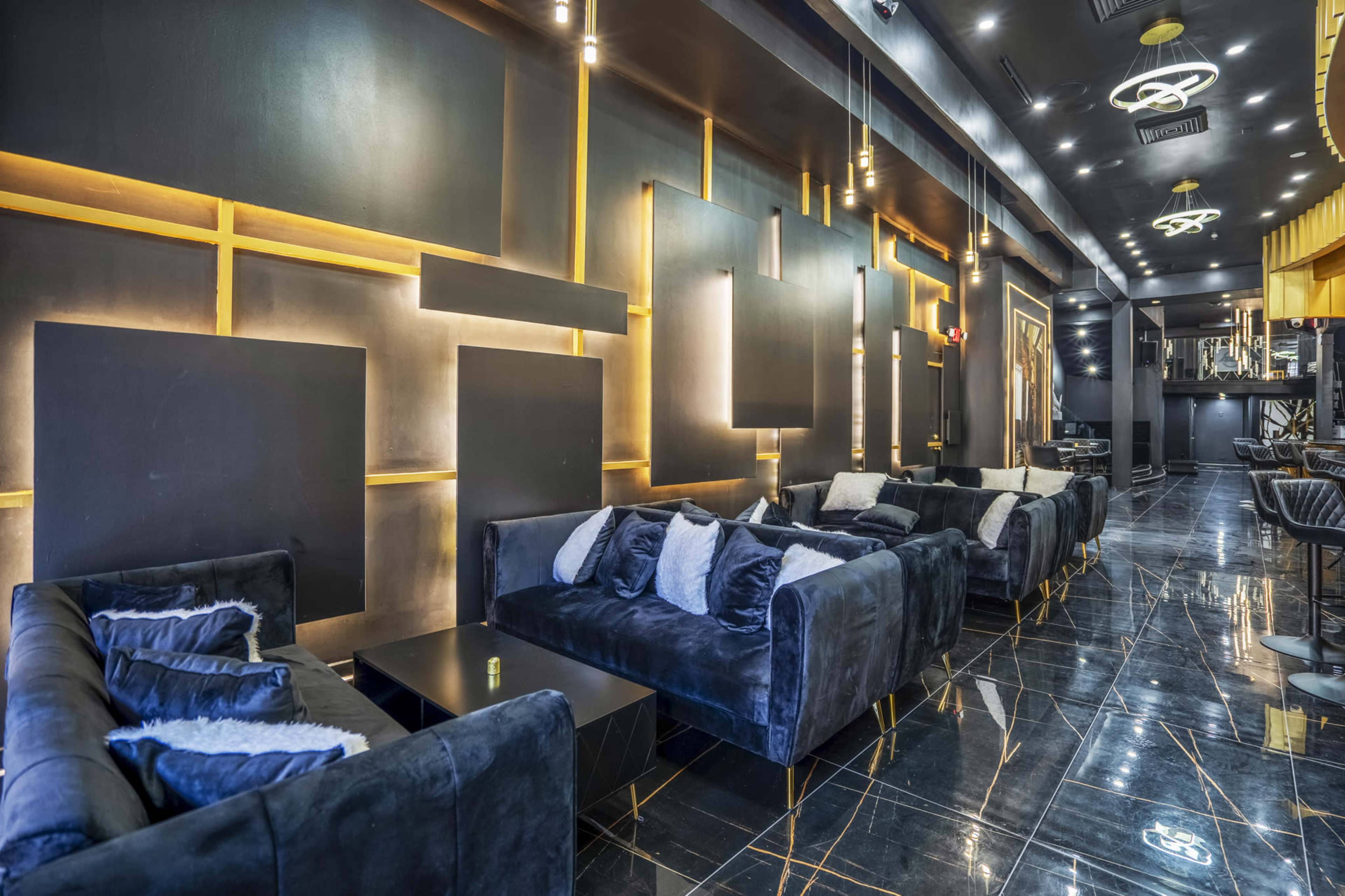 A modern lounge area with dark walls, black marble floors, and plush velvet sofas arranged along the space.