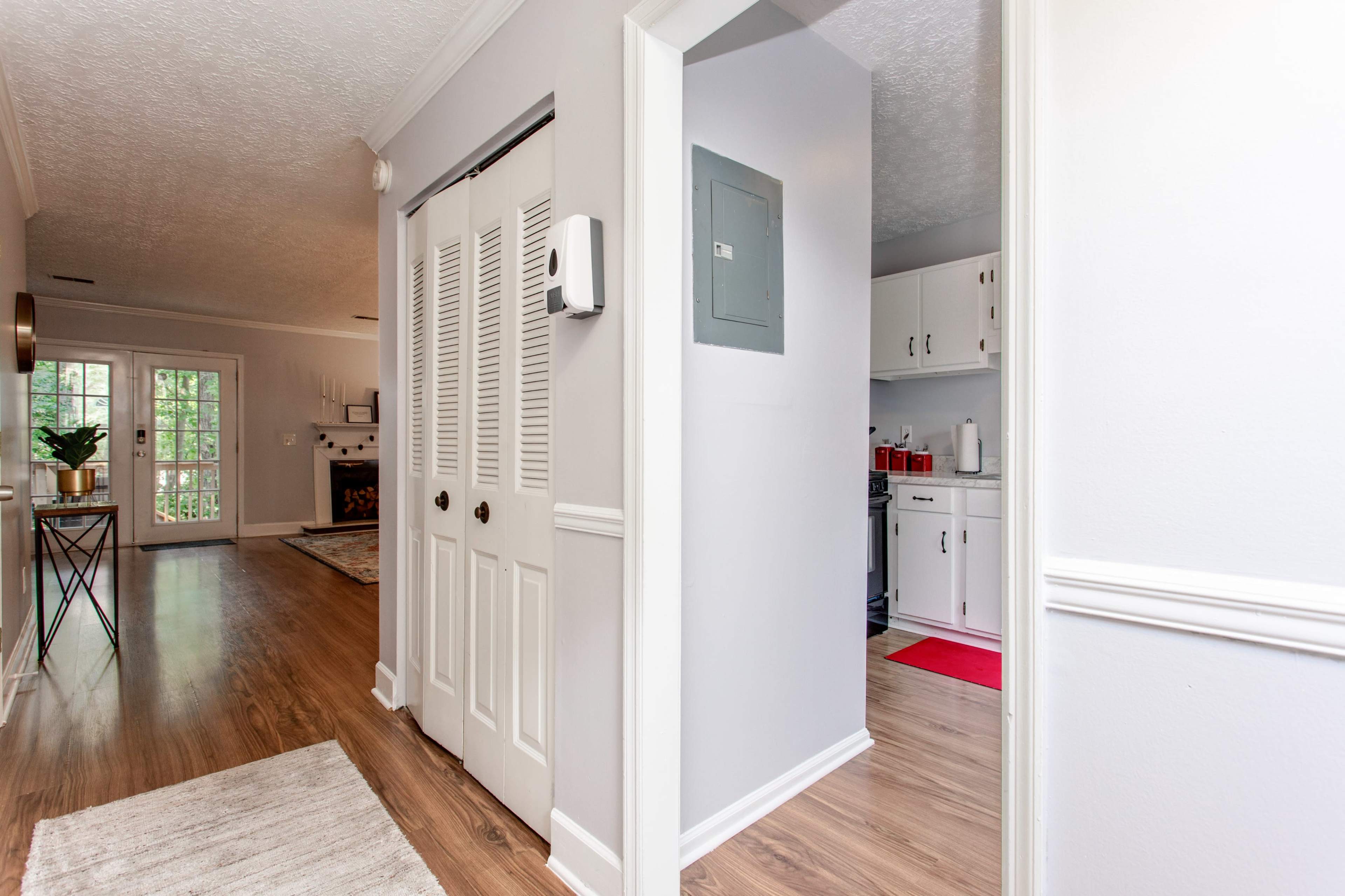 A hallway leading to a kitchen, with a pair of closed louvered doors on the left and a gray wall with an electrical panel to the right.