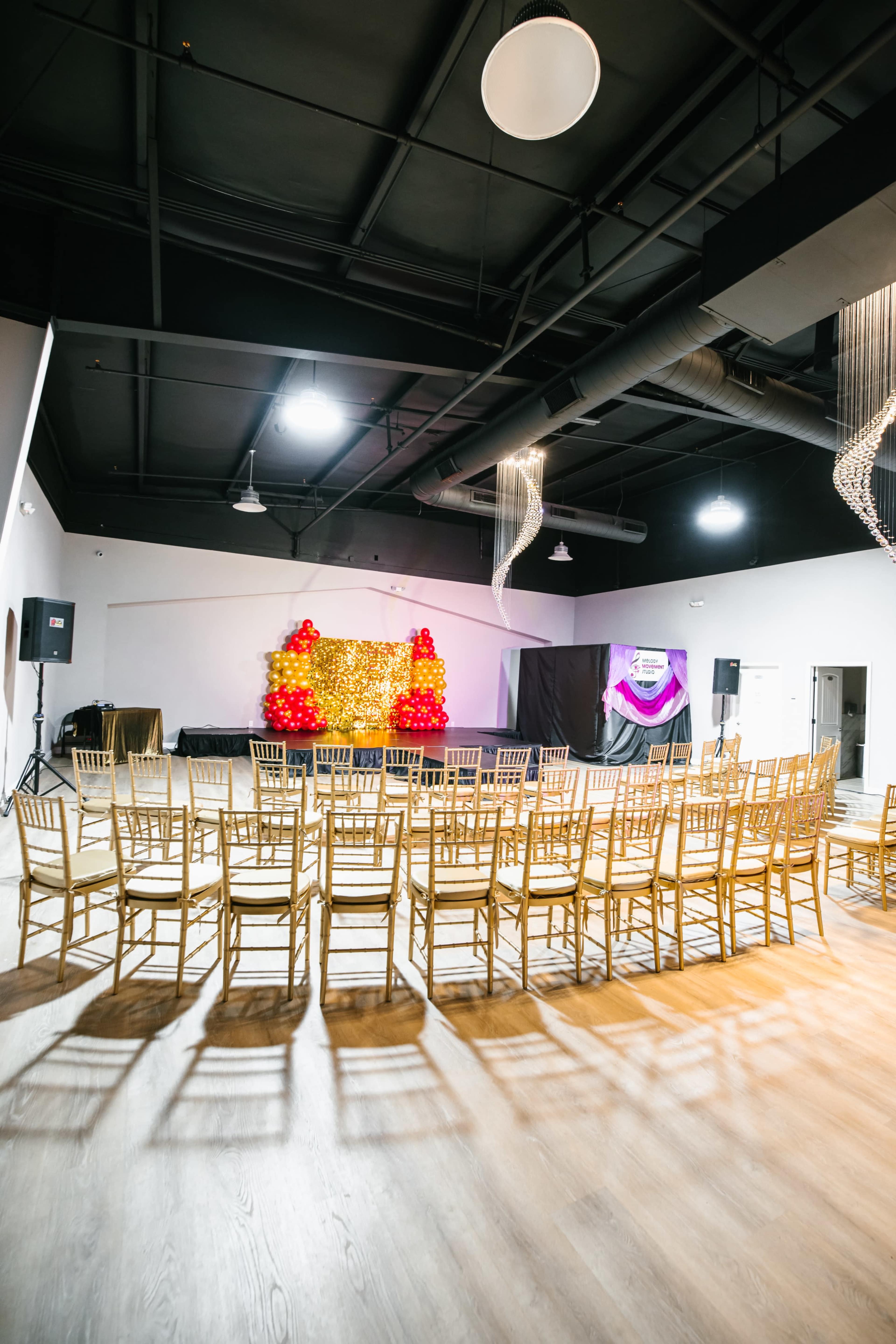 A spacious event venue features rows of gold chairs facing a decorated backdrop with red and gold elements.