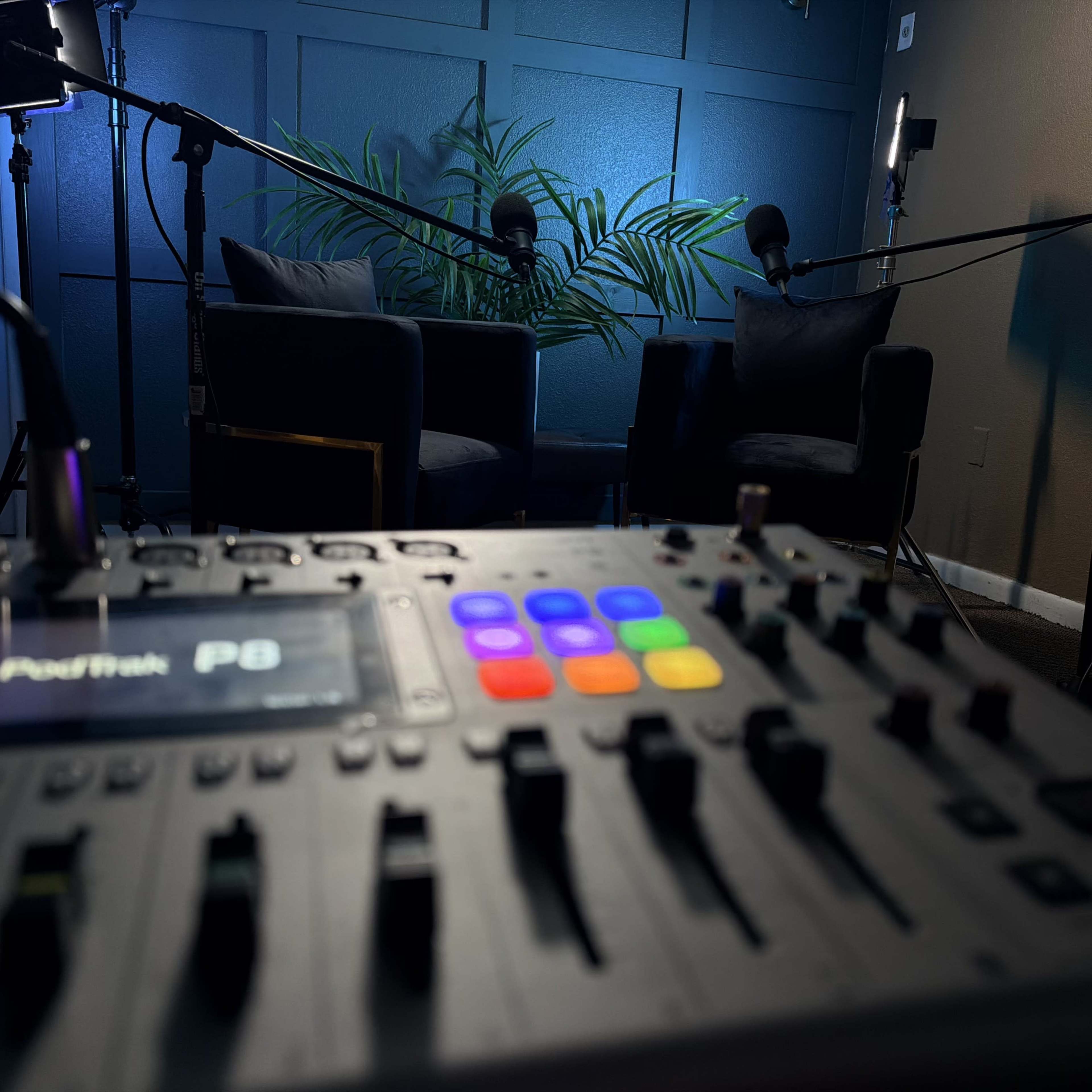 The image shows a podcasting setup featuring two chairs, microphones, and a sound mixer with colorful buttons in the foreground.