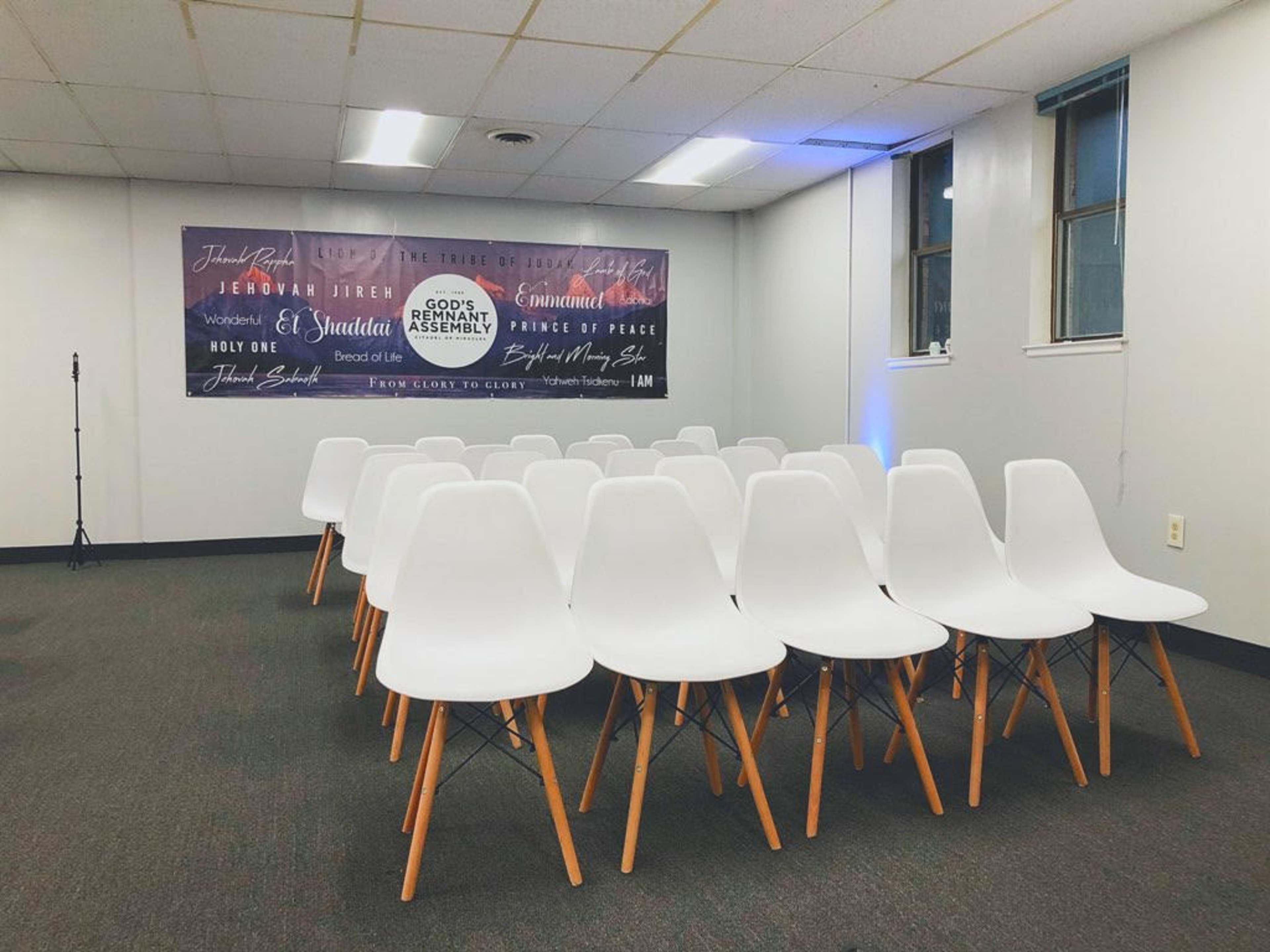 A room set up for an event, featuring several rows of white chairs facing a wall with promotional banners and a microphone in the corner.
