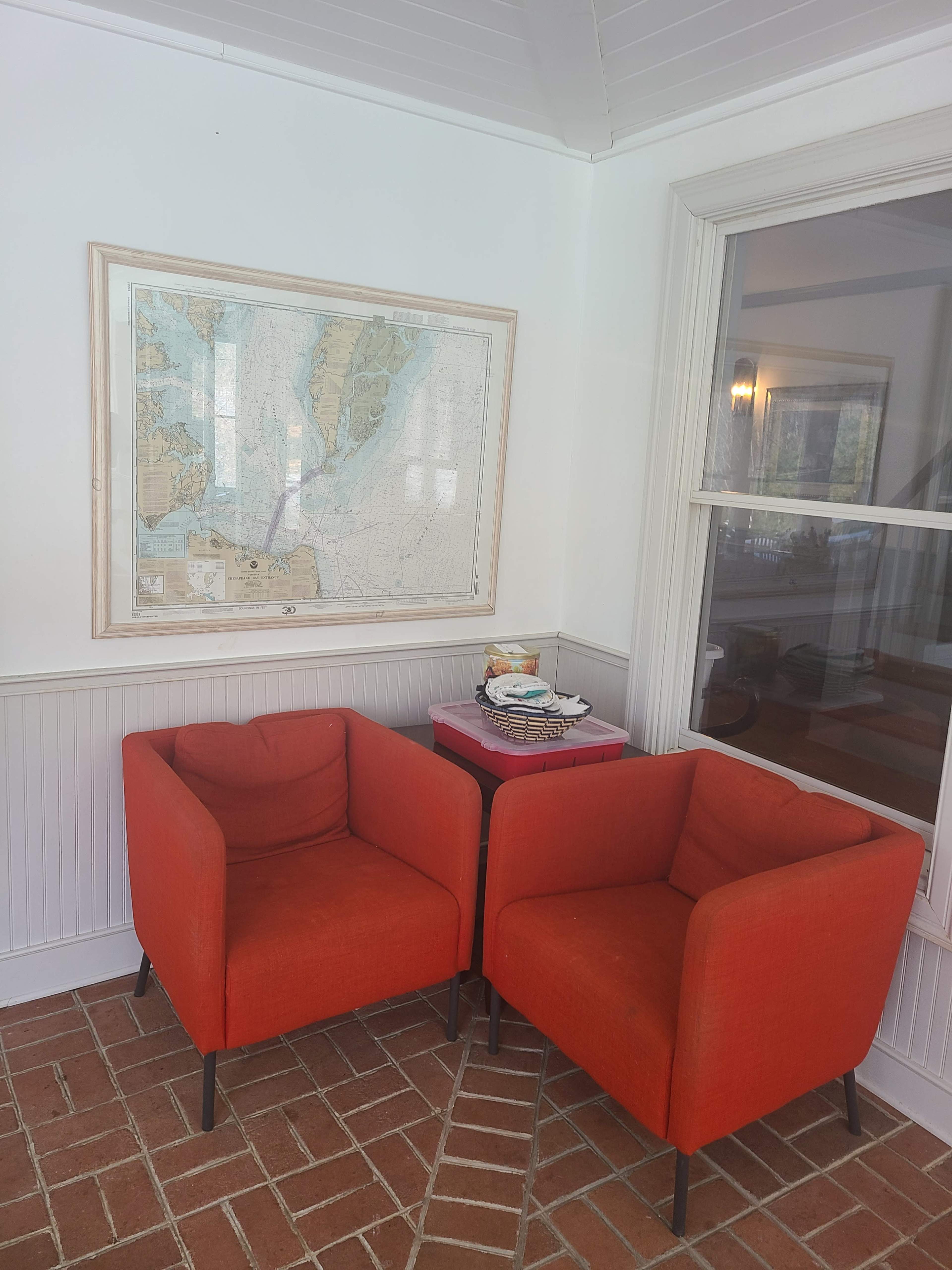 Two orange armchairs are positioned opposite each other near a map hung on the wall and a small table.