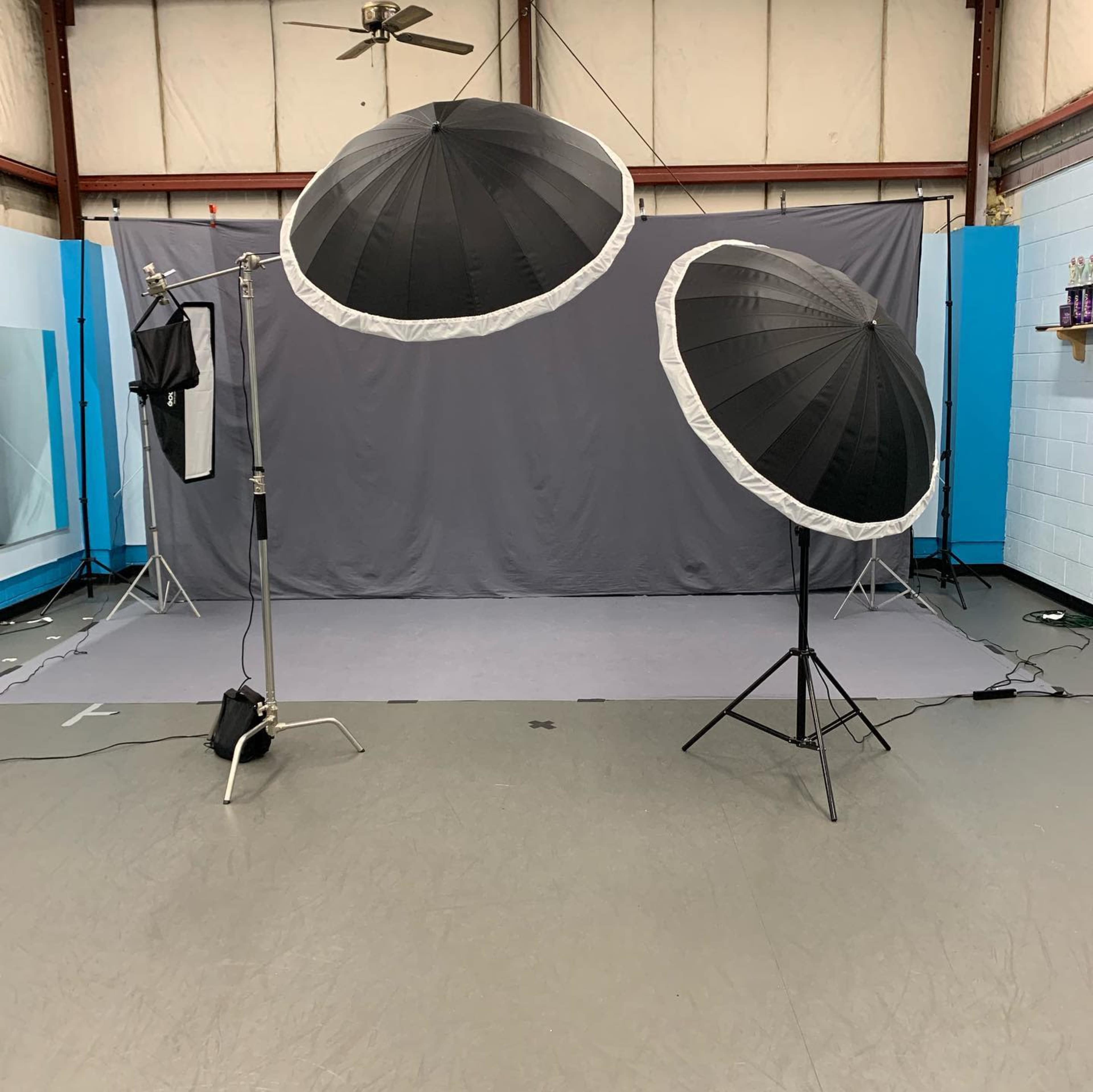A photography studio setup with two large umbrella softboxes positioned in front of a gray backdrop on a flat floor.