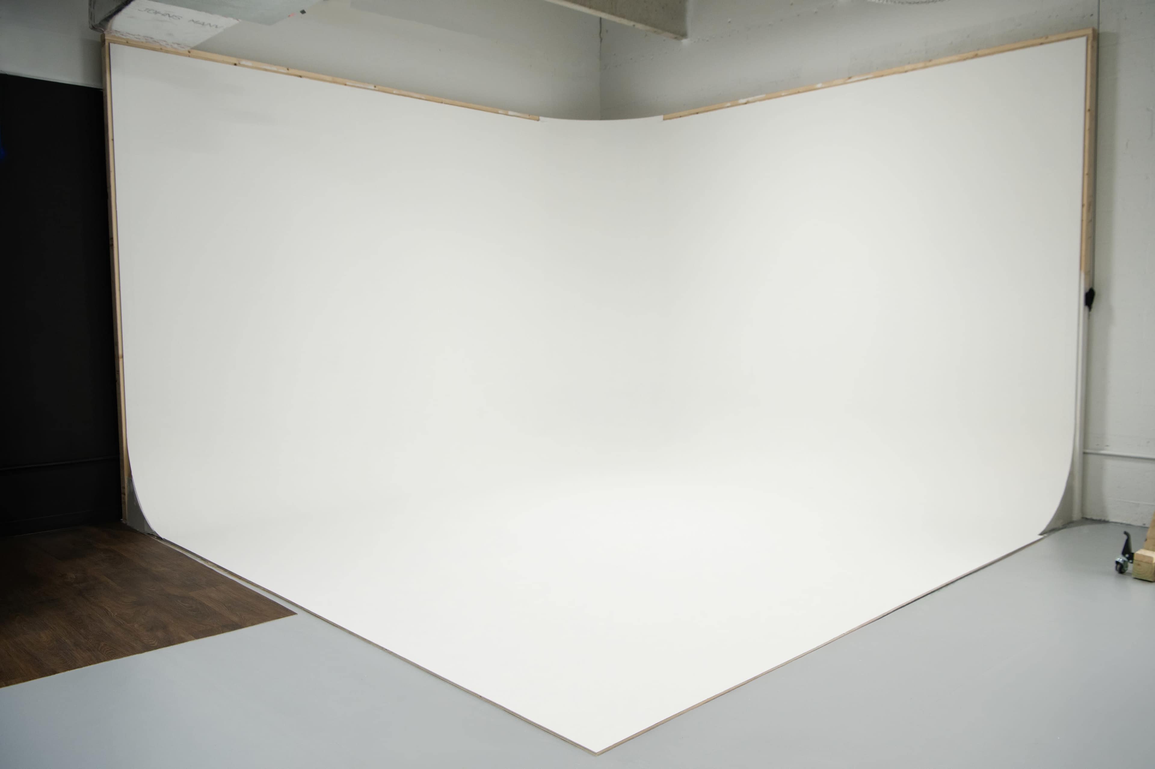 The image shows a photography studio with a seamless white backdrop and a clean floor setup.