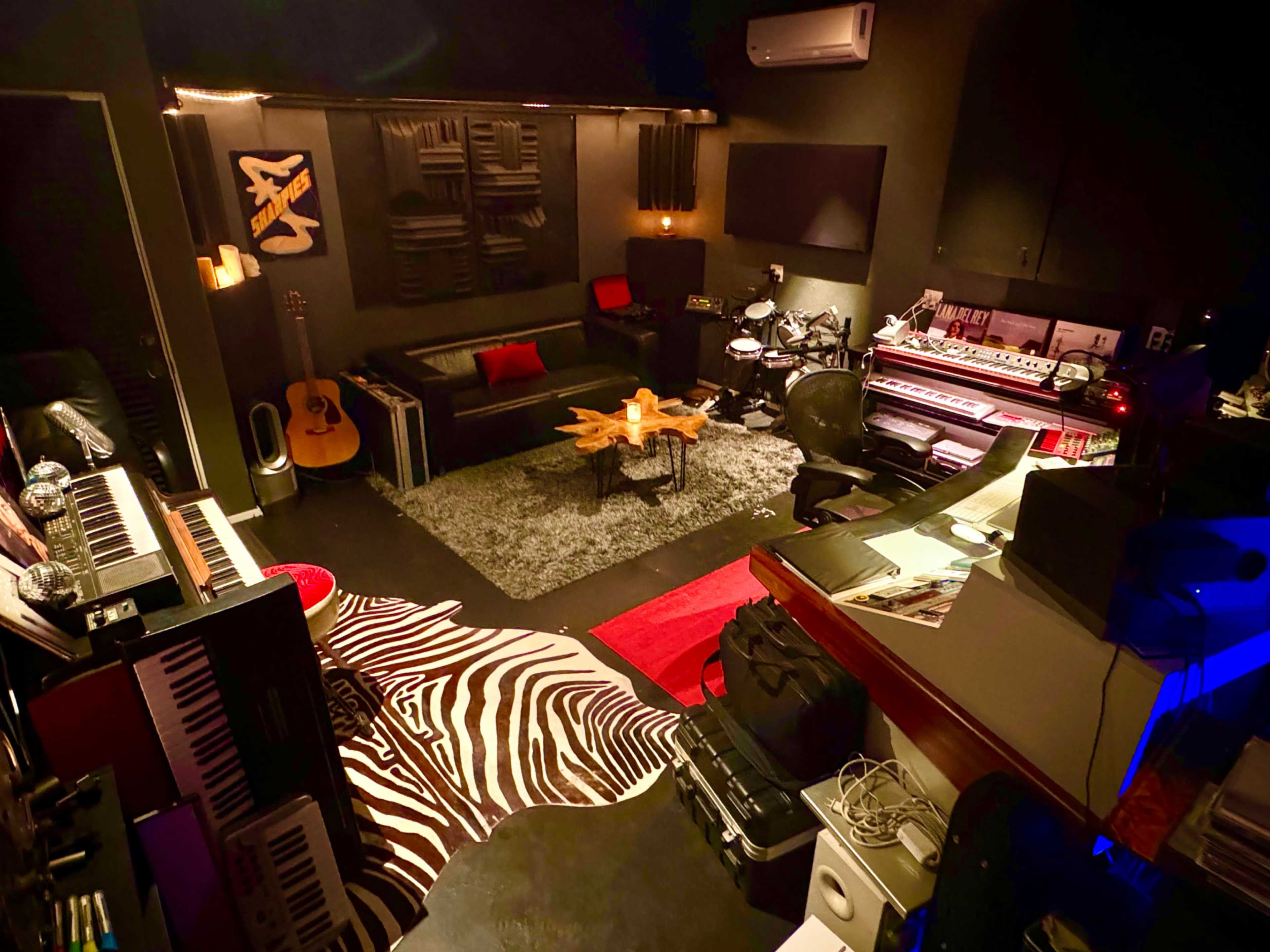 The image shows a recording studio with various musical instruments, a black and white zebra-patterned rug, and a central coffee table surrounded by seating areas.