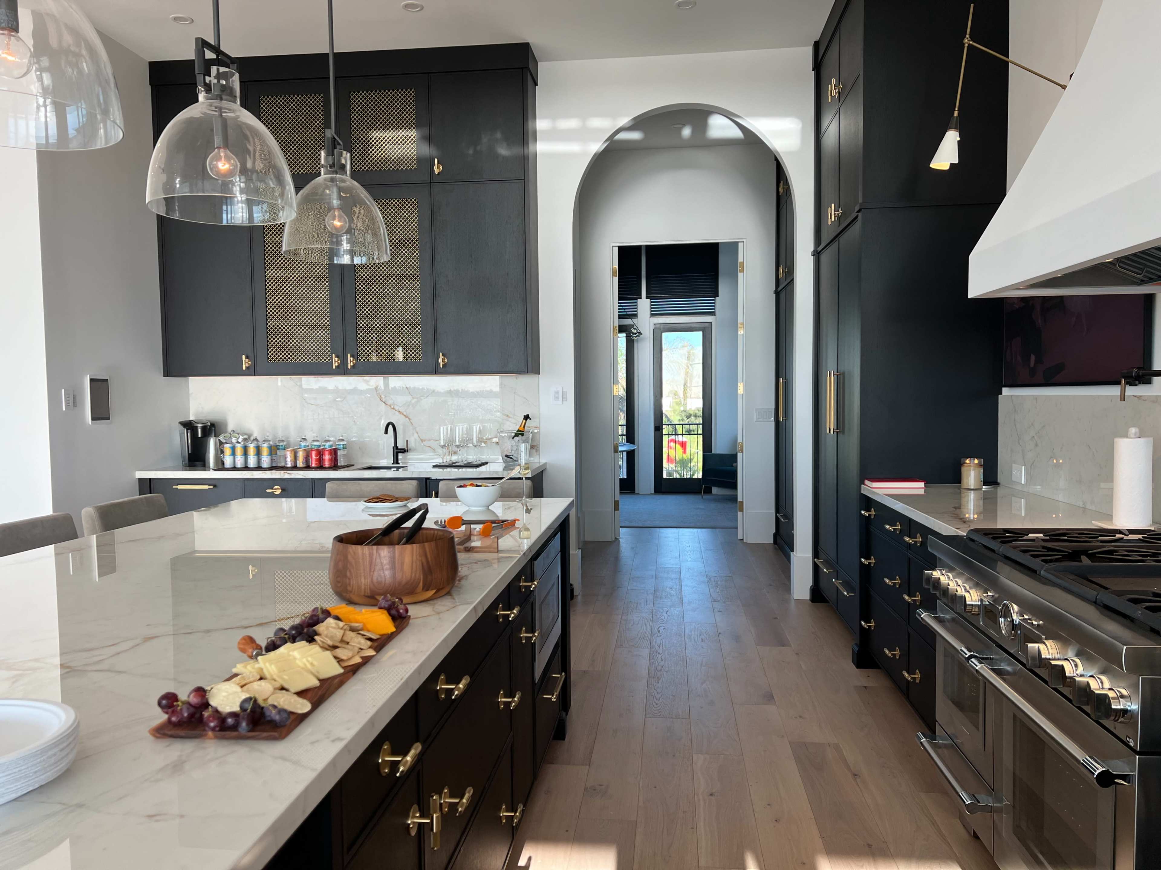 A modern kitchen features dark cabinetry, a marble countertop with a charcuterie board, and large pendant lights above the island.