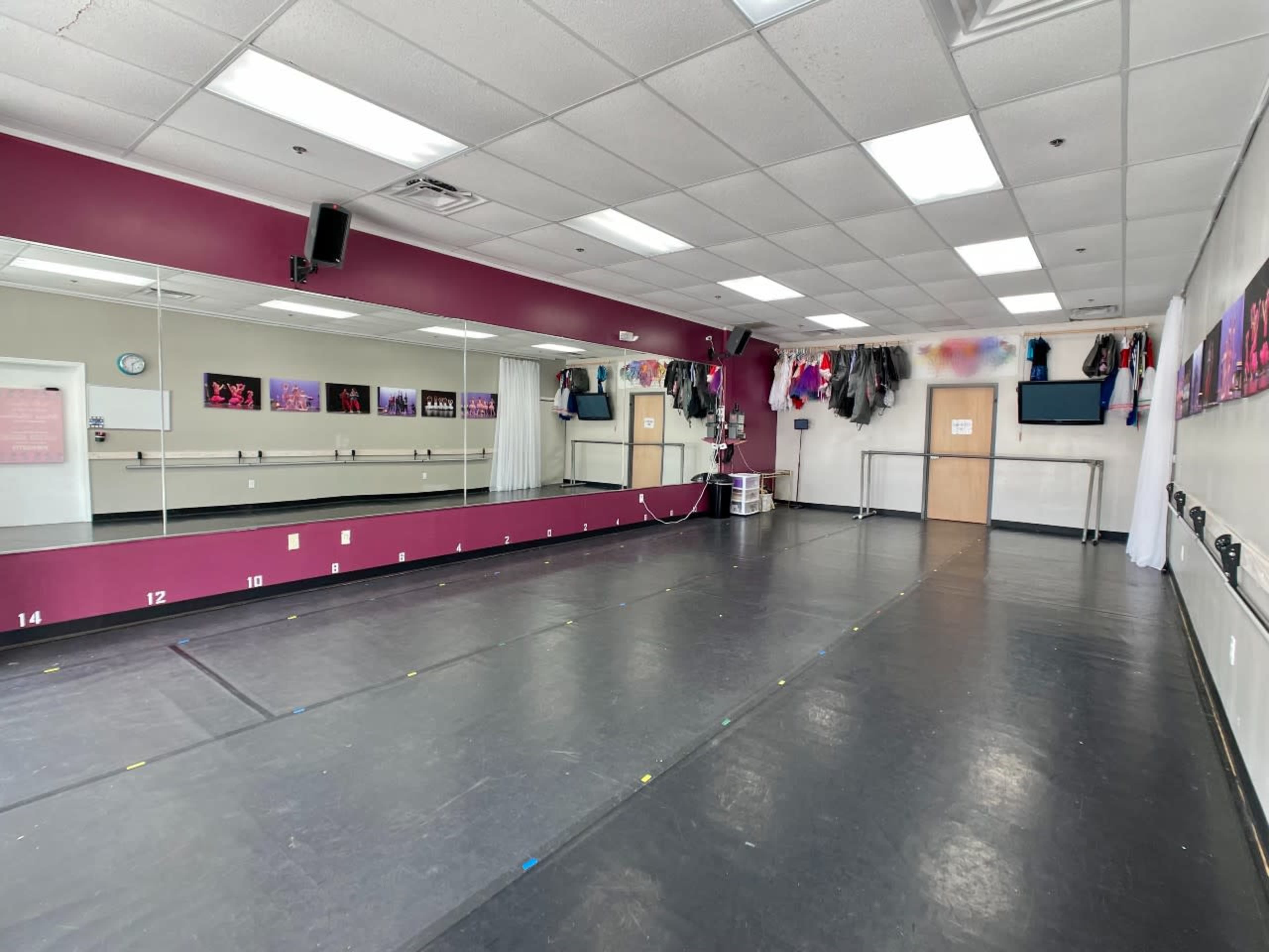 A spacious dance studio with a mirrored wall, a dark floor, and various costumes hanging on the walls.