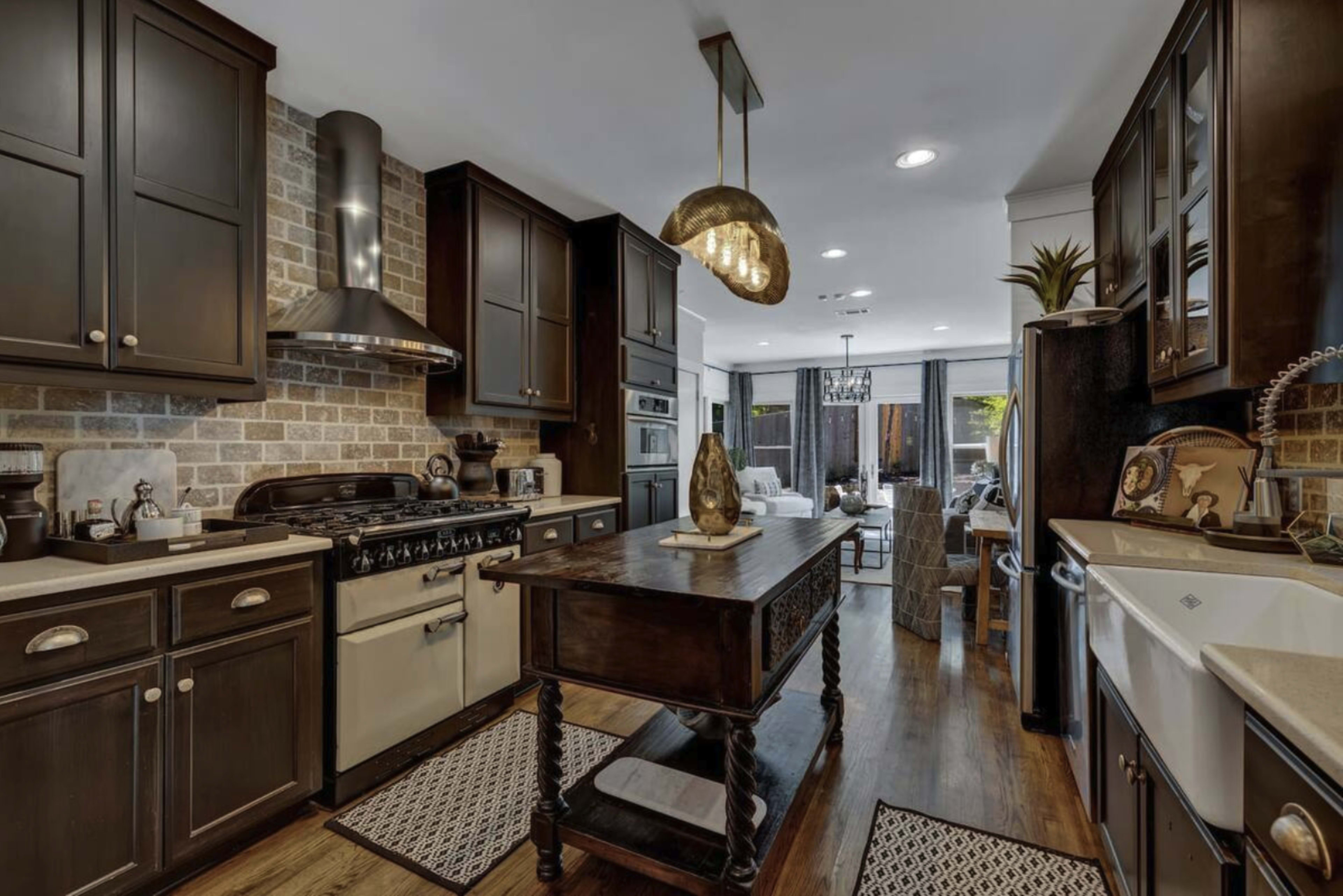 A modern kitchen features dark cabinetry, a vintage-style stove, a central wooden island, and a mix of stone and hardwood flooring.