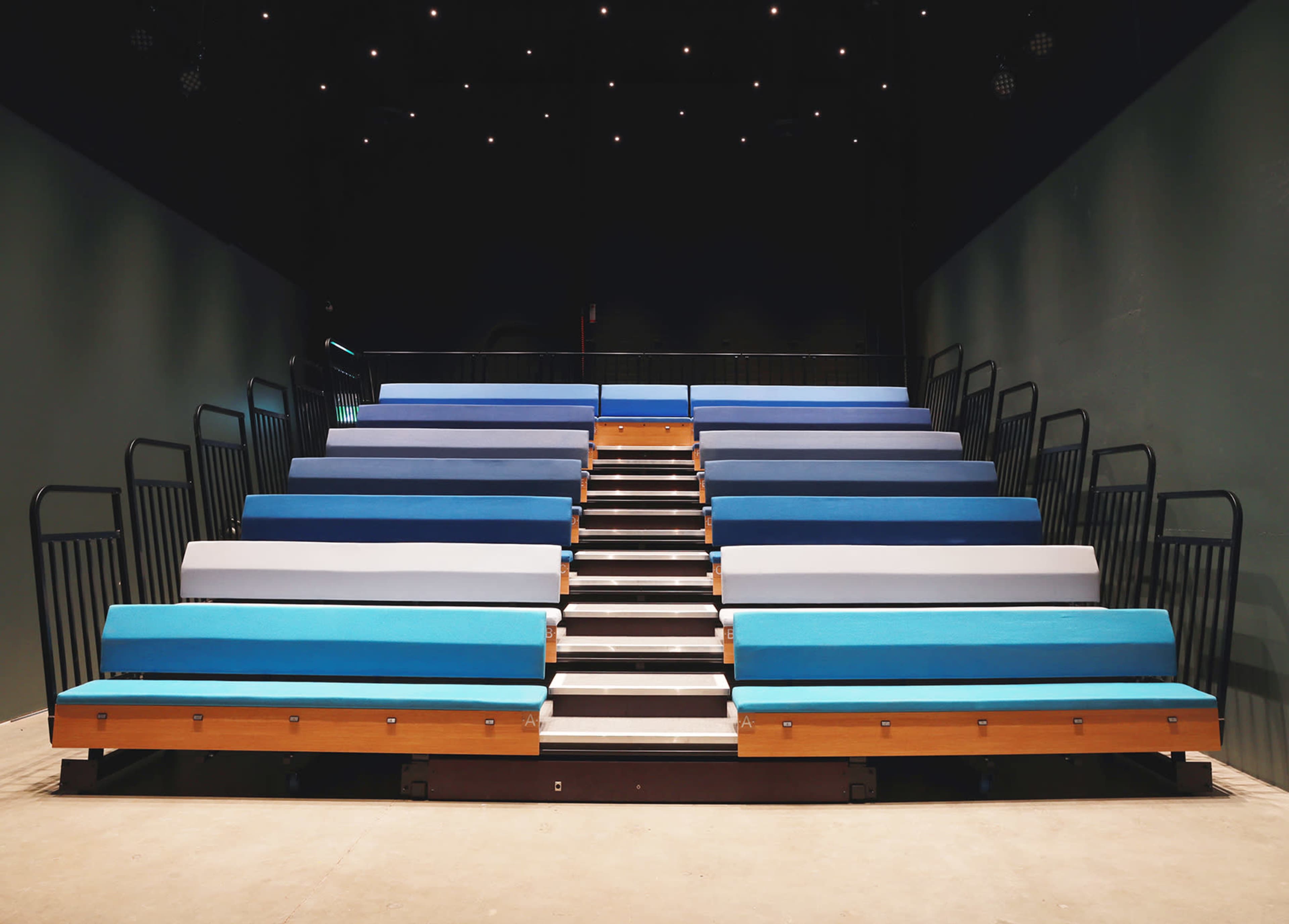 A tiered seating arrangement with blue and gray benches in a dimly lit theater.