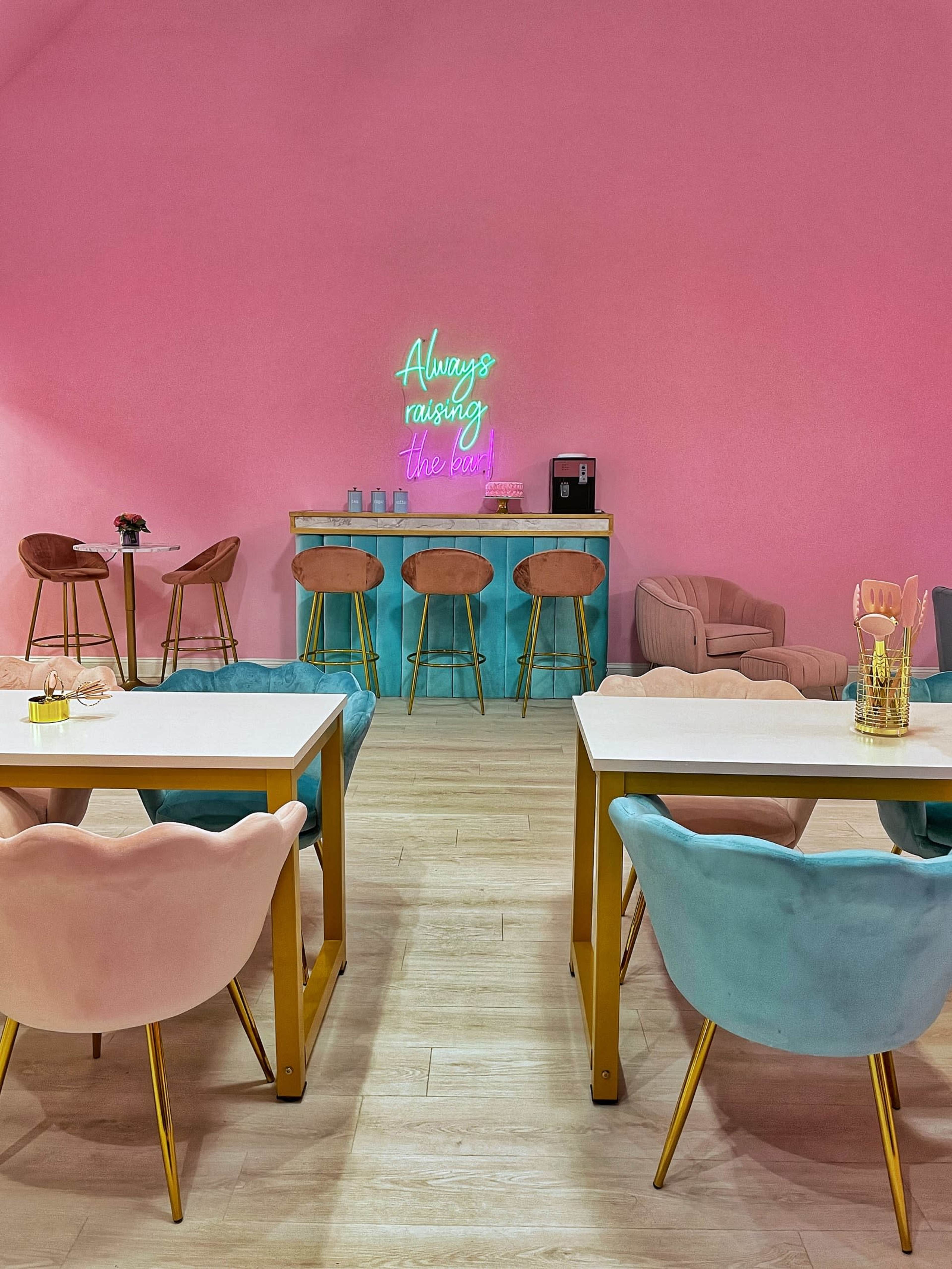 A pastel-colored interior features pink walls, a bar with teal accents, and various stylish seating arrangements.