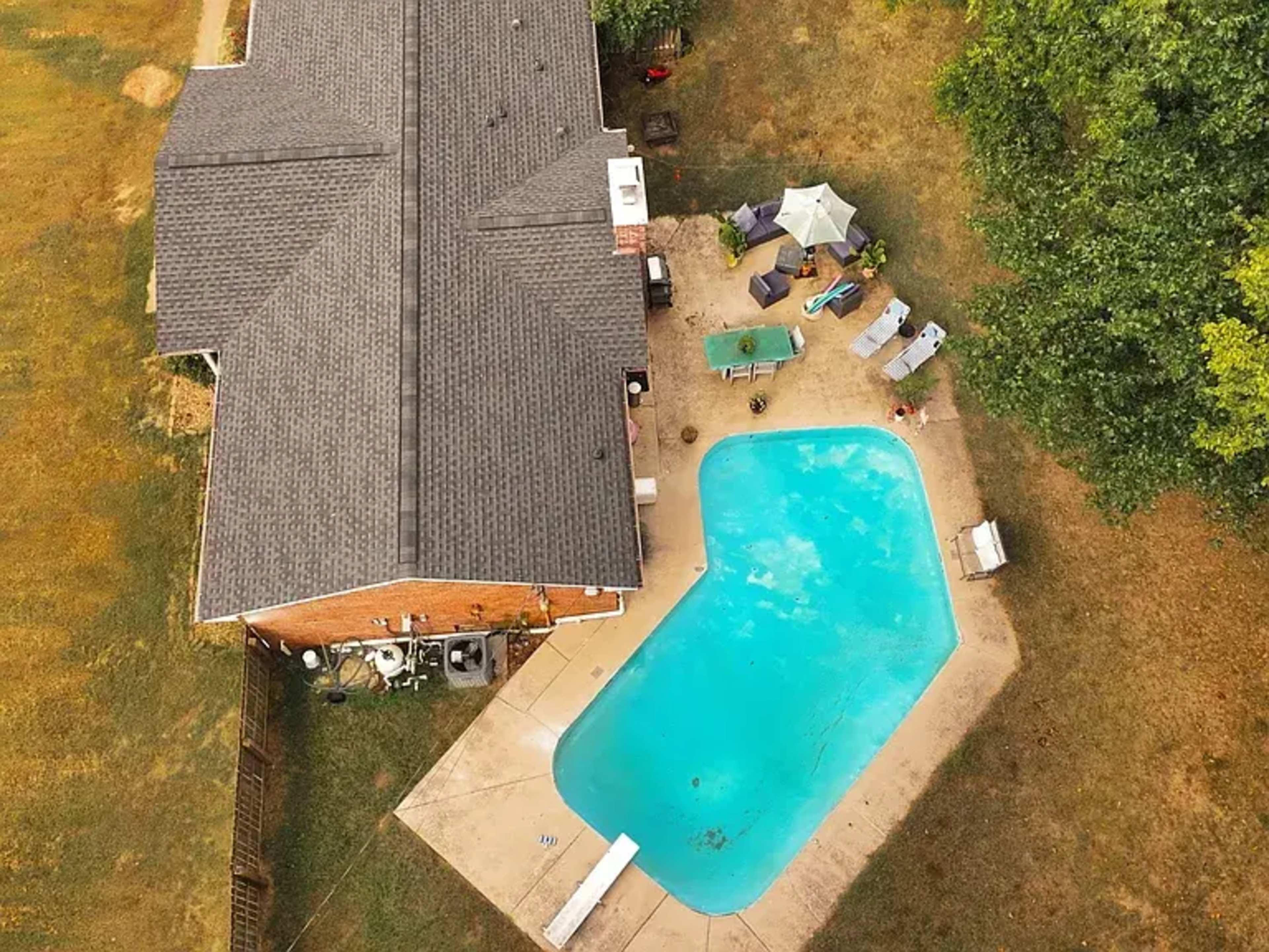 The image shows an aerial view of a house with a pool and a patio area surrounded by grass.