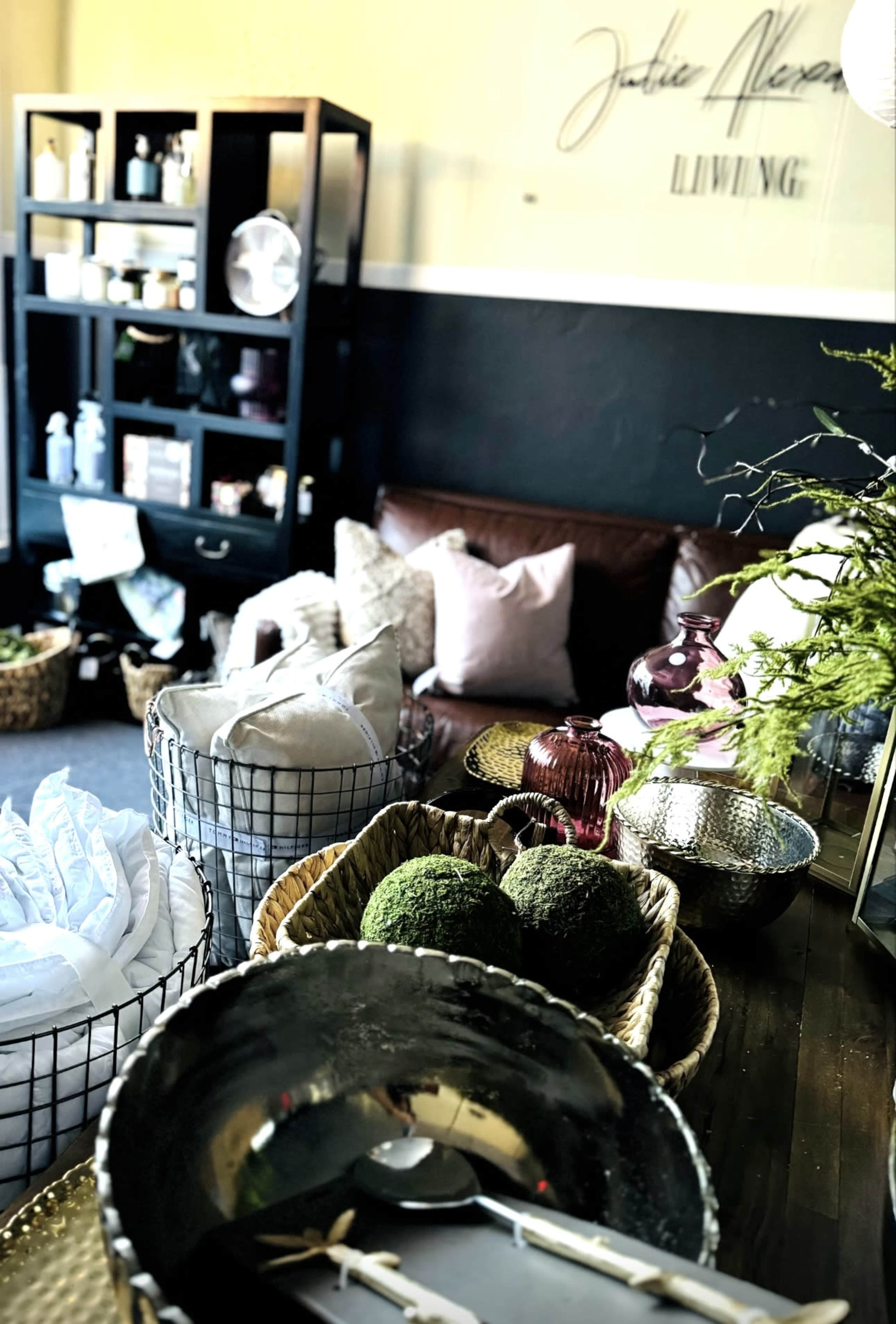 A cozy room featuring a brown leather sofa, decorative baskets filled with various items, and a black shelf displaying containers and plants.