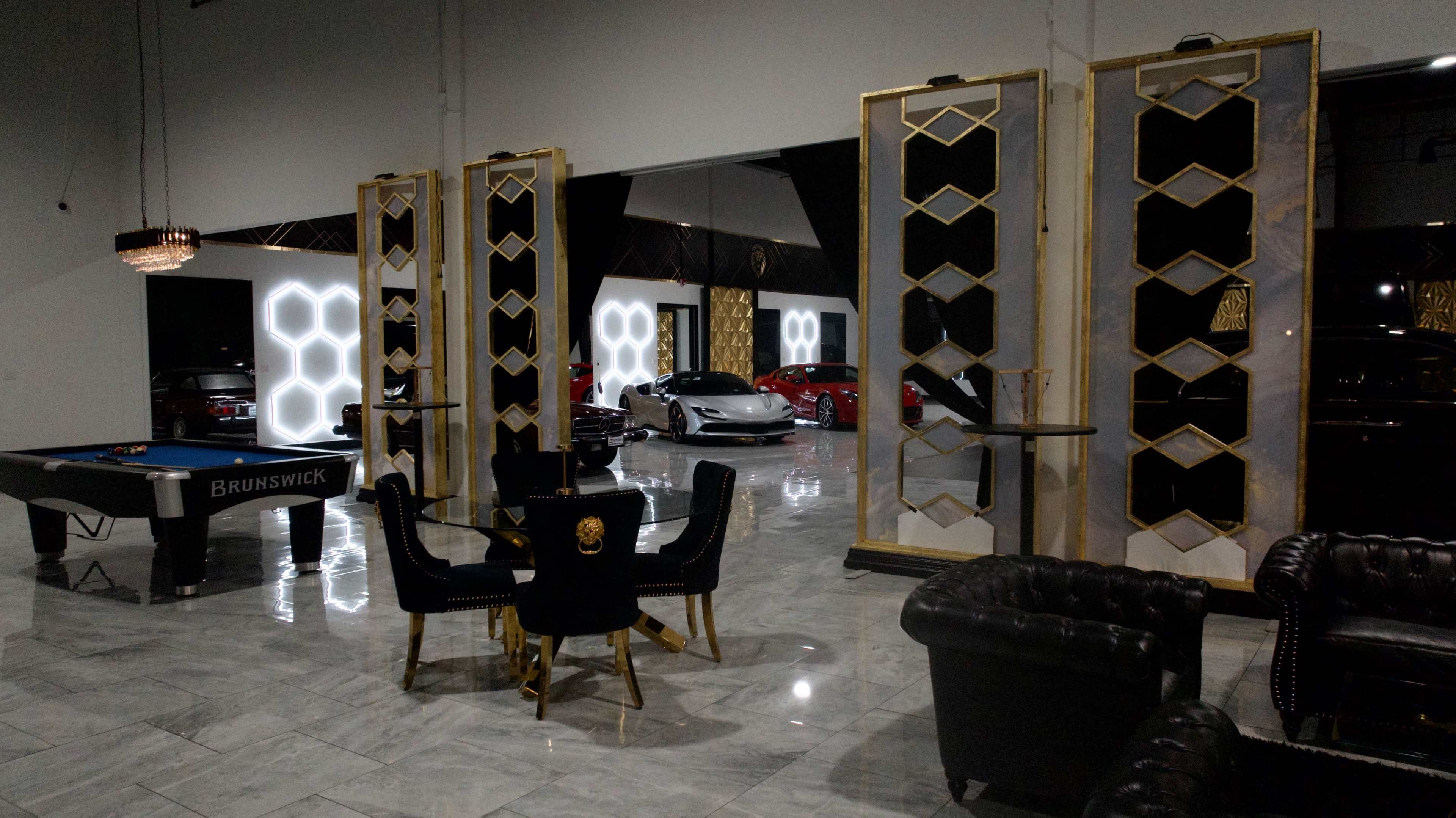 The image shows a luxurious interior featuring a pool table, a dining set, and two large decorative panels, with several cars visible in a well-lit garage area.