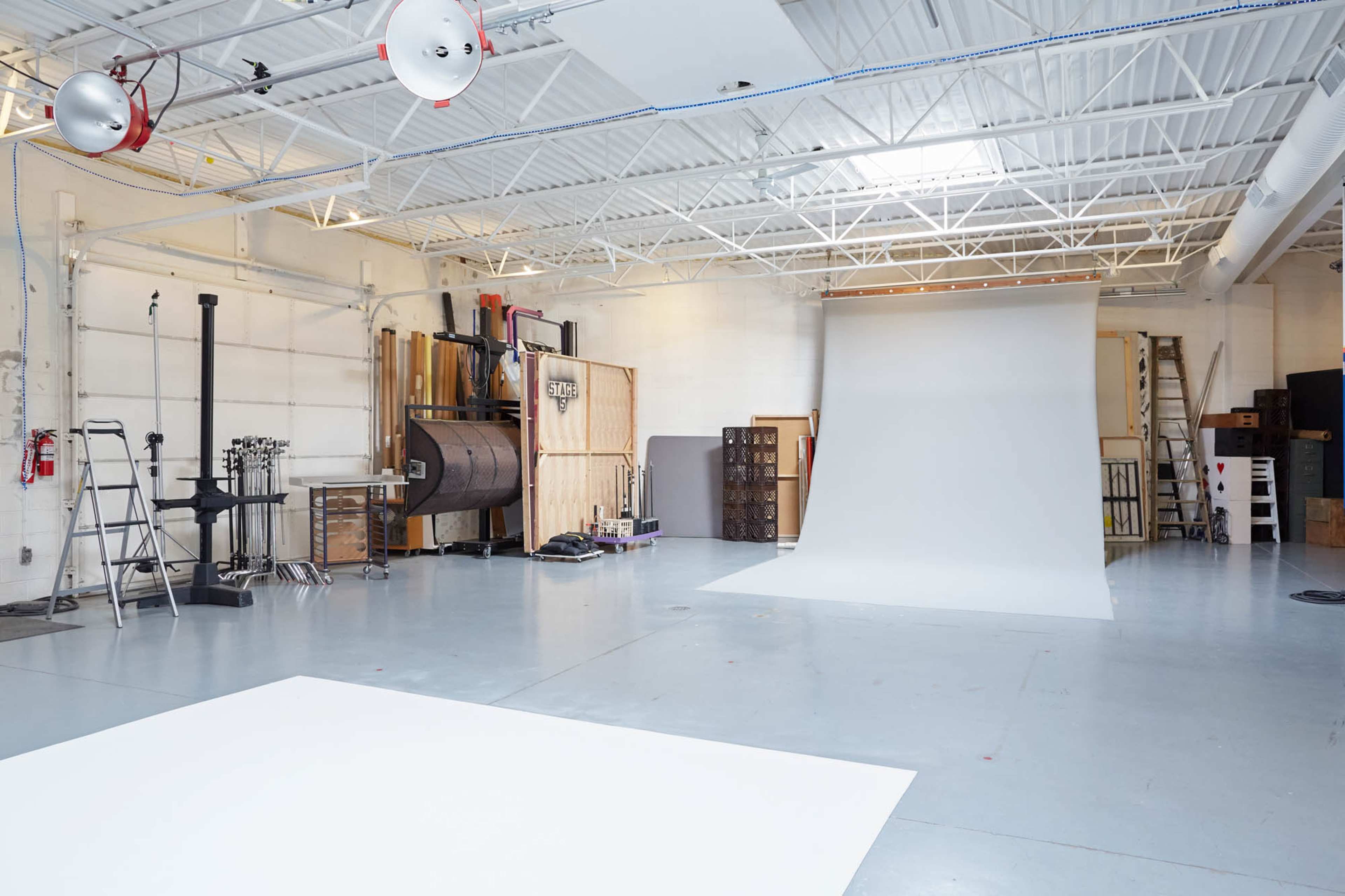 A spacious photography studio with a white backdrop, lighting equipment, and various tools along the walls.
