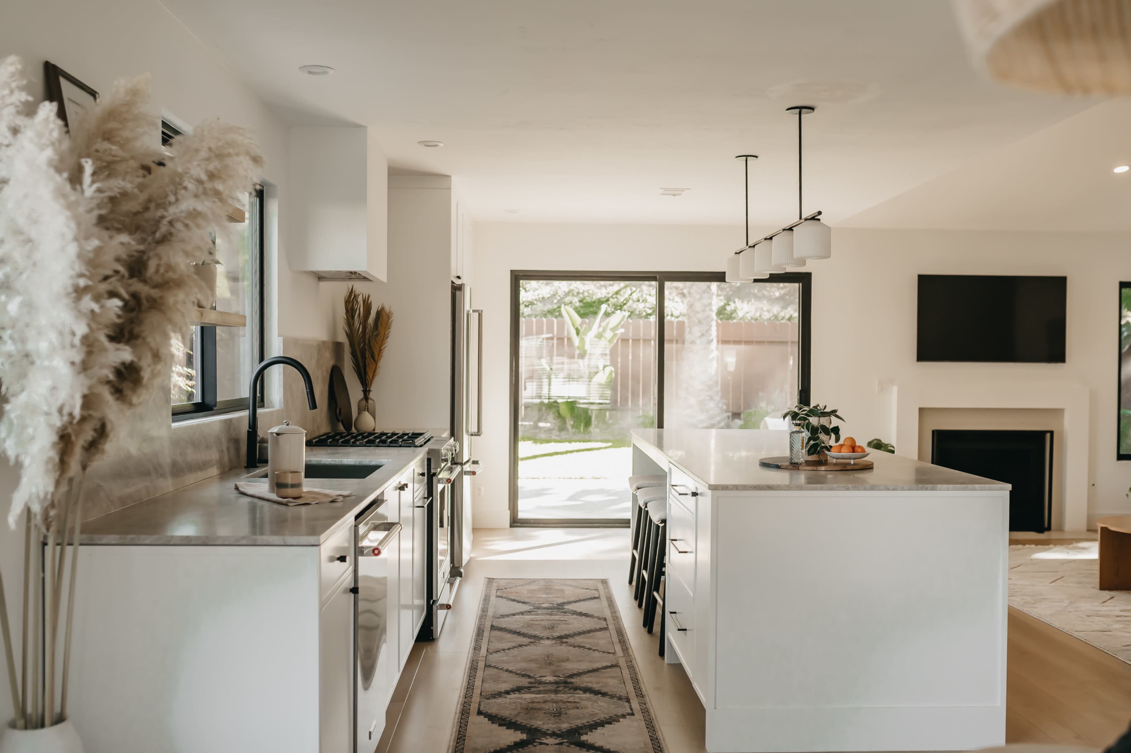 A modern kitchen features white cabinetry, a large island, and glass doors that open to a backyard.
