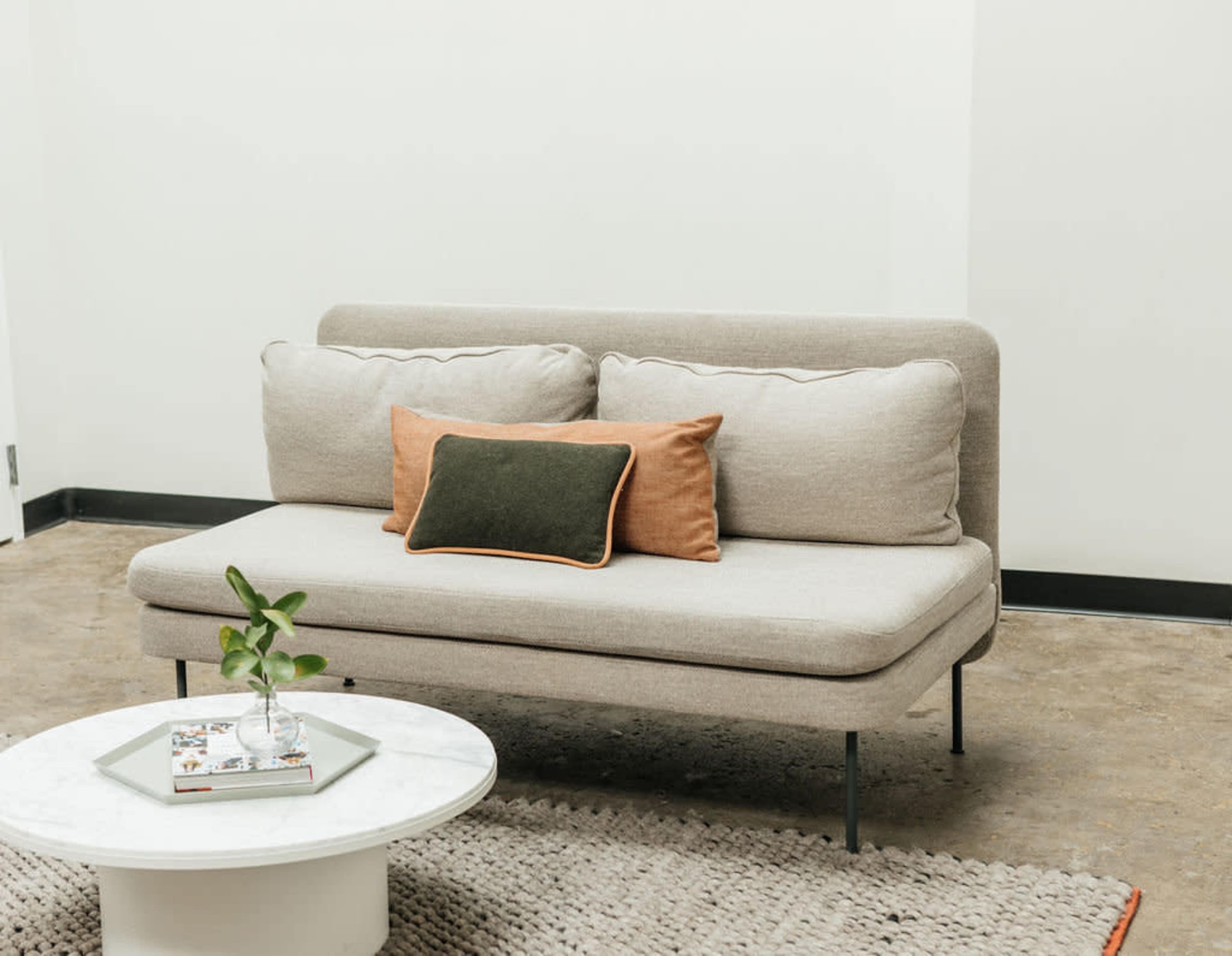 A light gray couch with three cushions is positioned next to a round marble coffee table on a beige rug in a minimalist room.