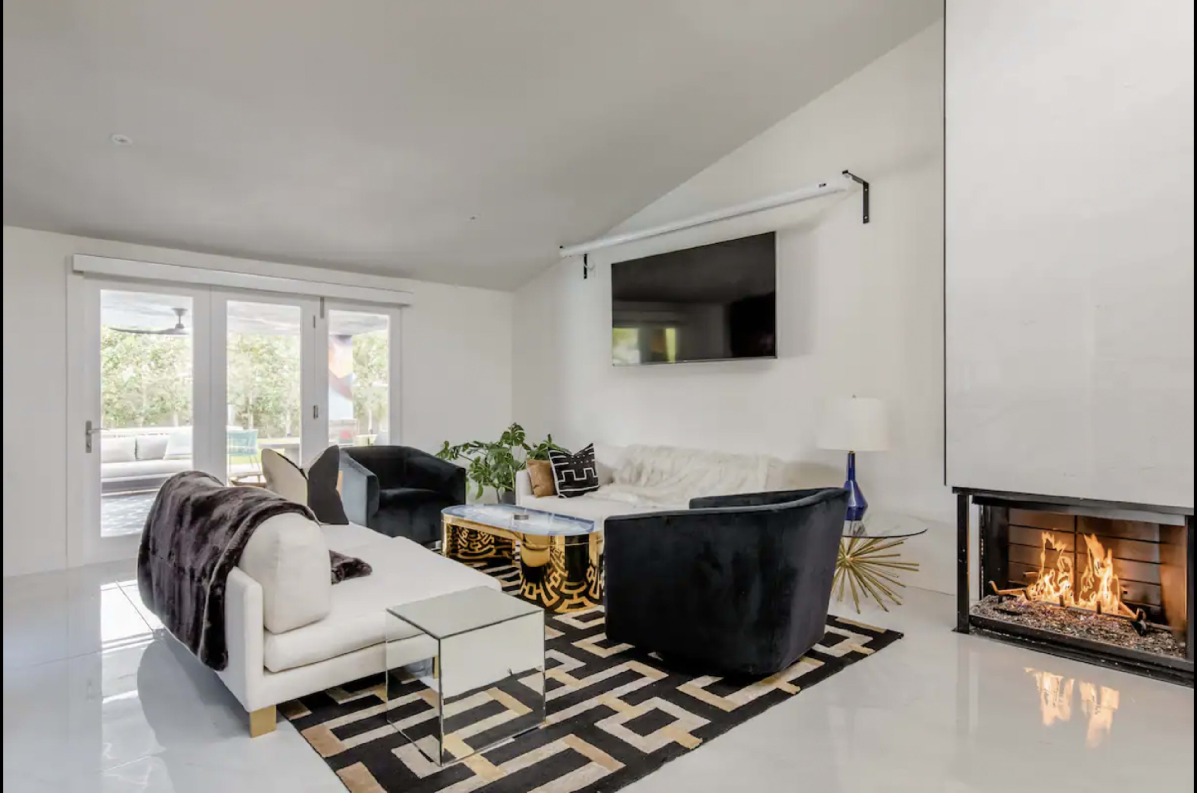 A modern living room with a white sofa, black armchairs, a geometric rug, and a fireplace.