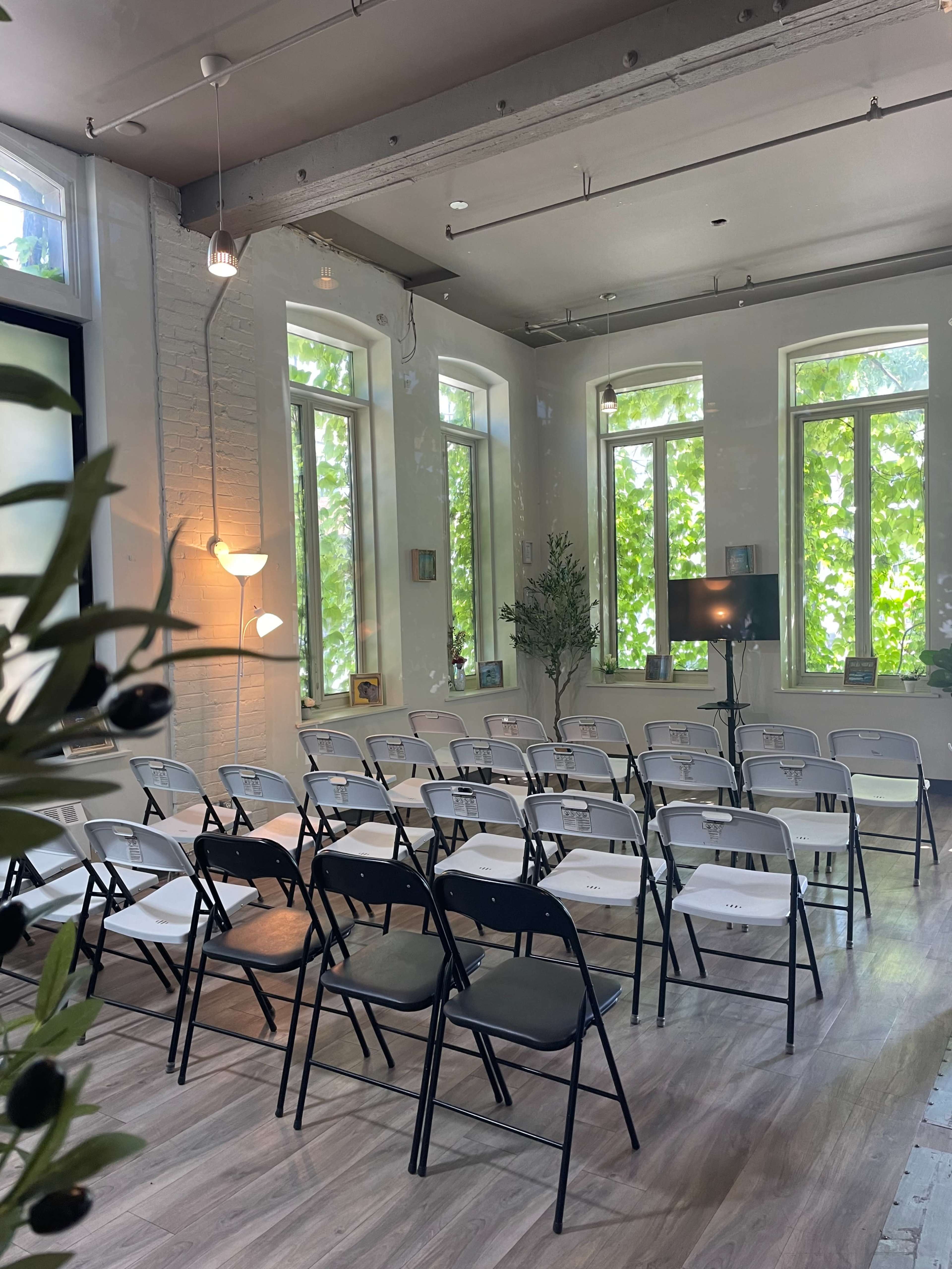A group of neatly arranged black and white folding chairs in a well-lit room with large windows and a decorative plant.