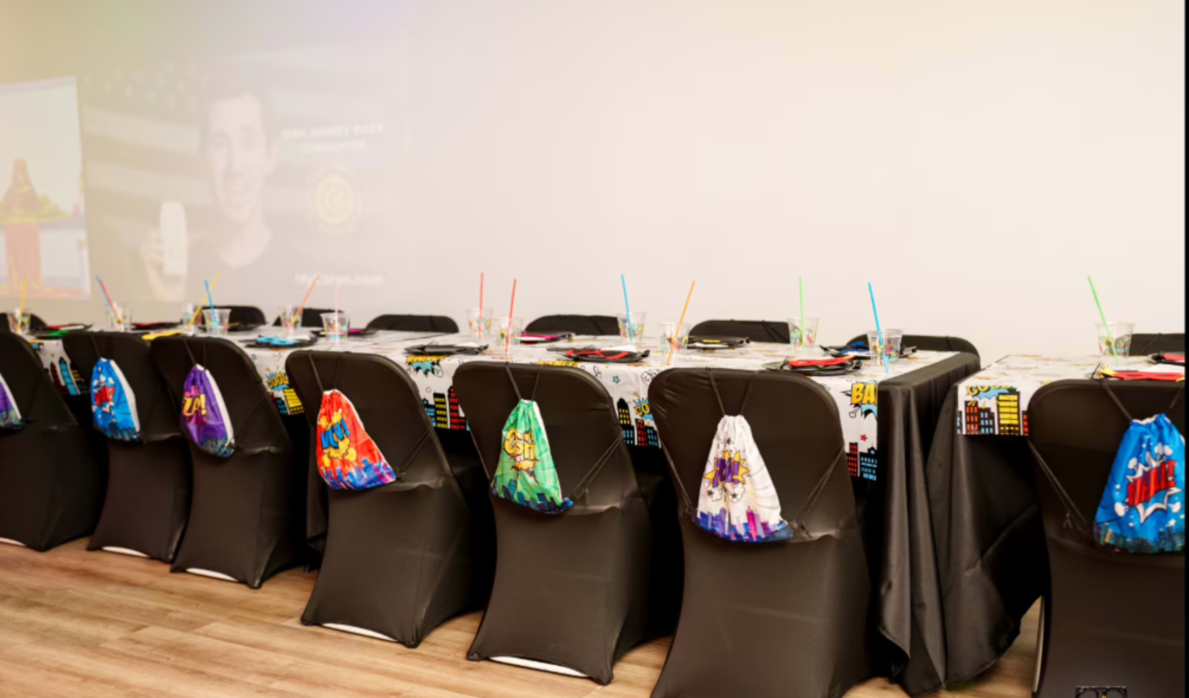 A long table is set up with colorful tableware and decorative bags hanging from the chairs, ready for a festive gathering.