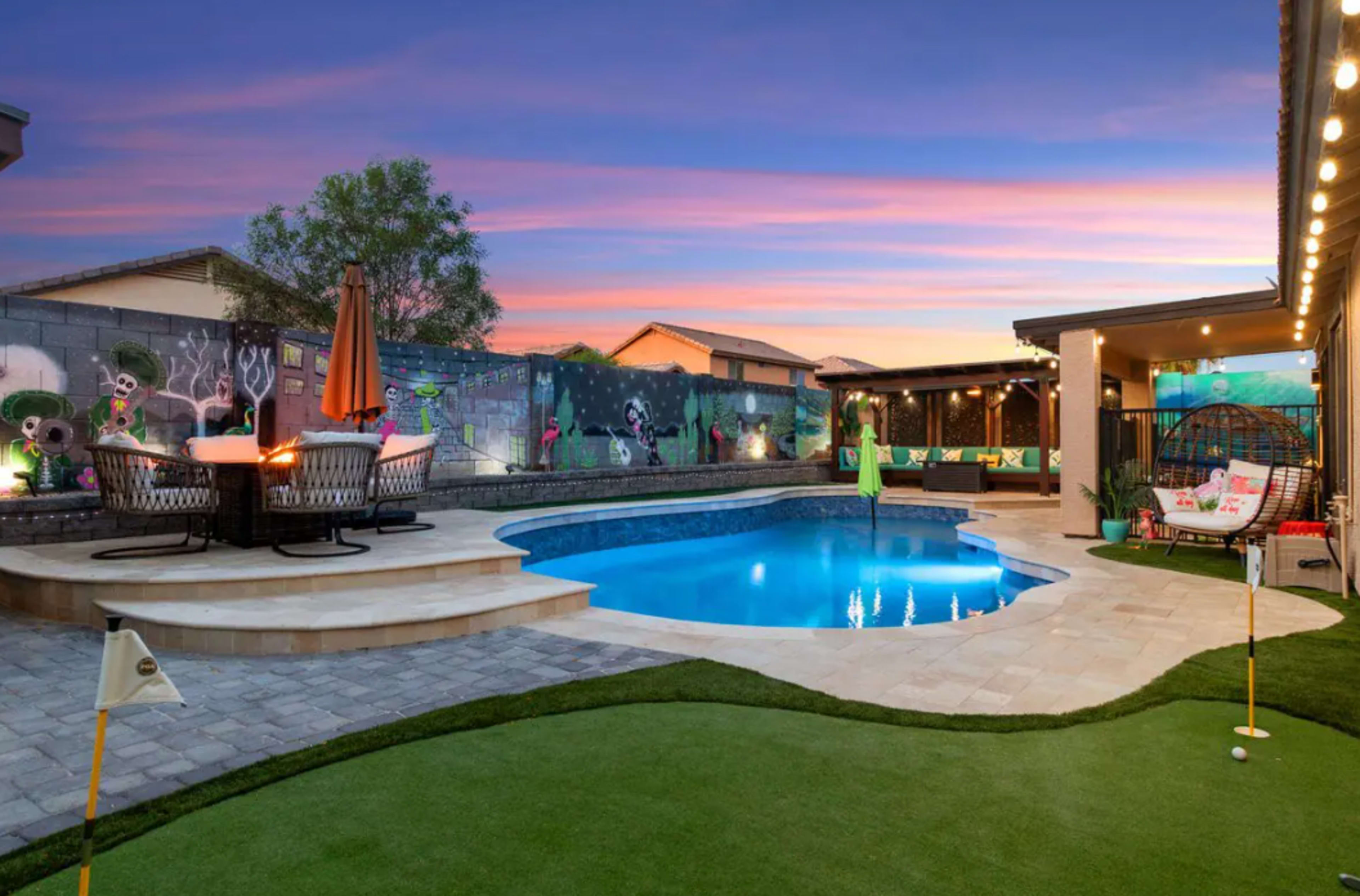 A backyard oasis featuring a swimming pool, a patio with seating, and a vibrant mural on the surrounding walls.