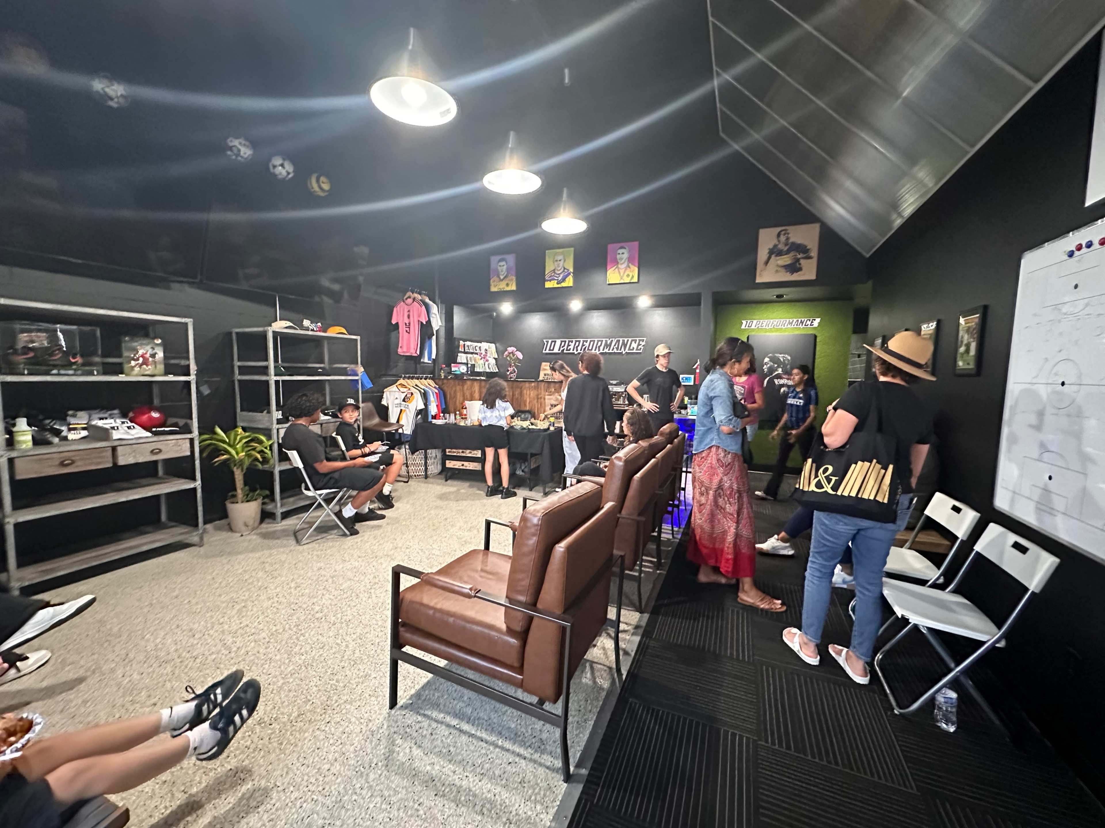 A group of people are engaged in discussion in a room featuring sports apparel displays and seating arranged around a central area.