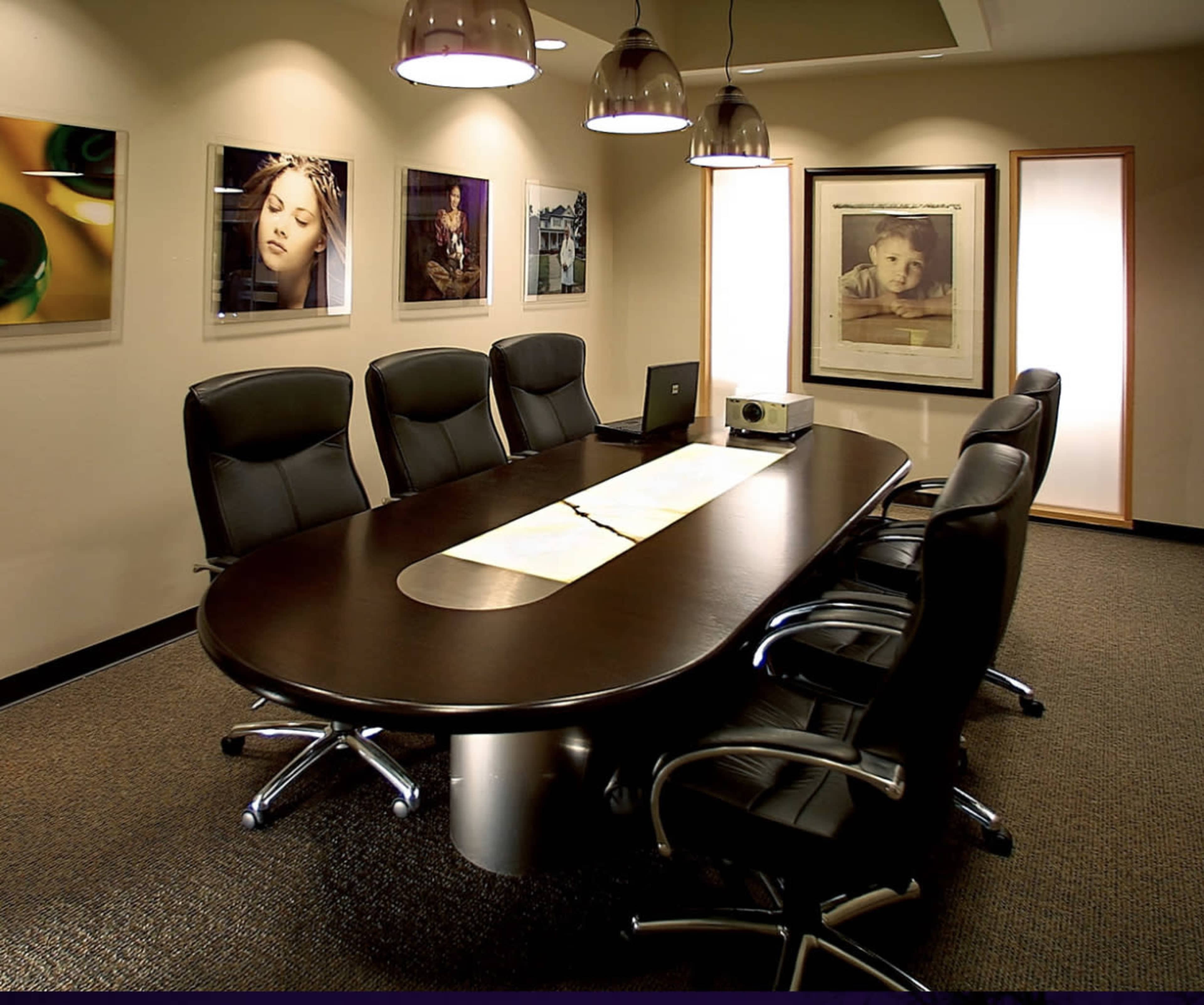 A conference room features an oval table surrounded by black leather chairs, with framed photographs displayed on the walls.