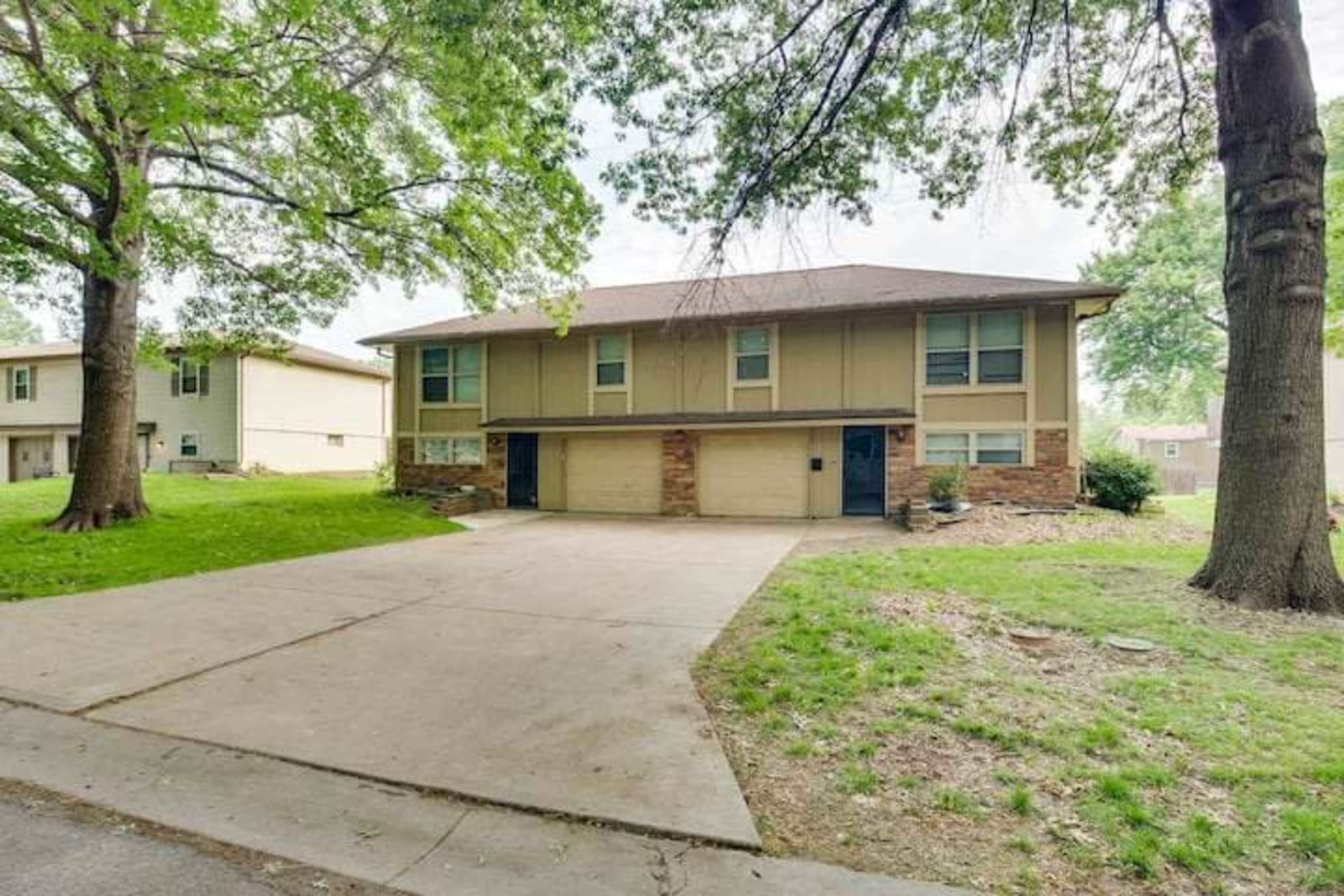 A two-story house with a brick and siding exterior features a double garage and is set on a grassy lot with large trees nearby.