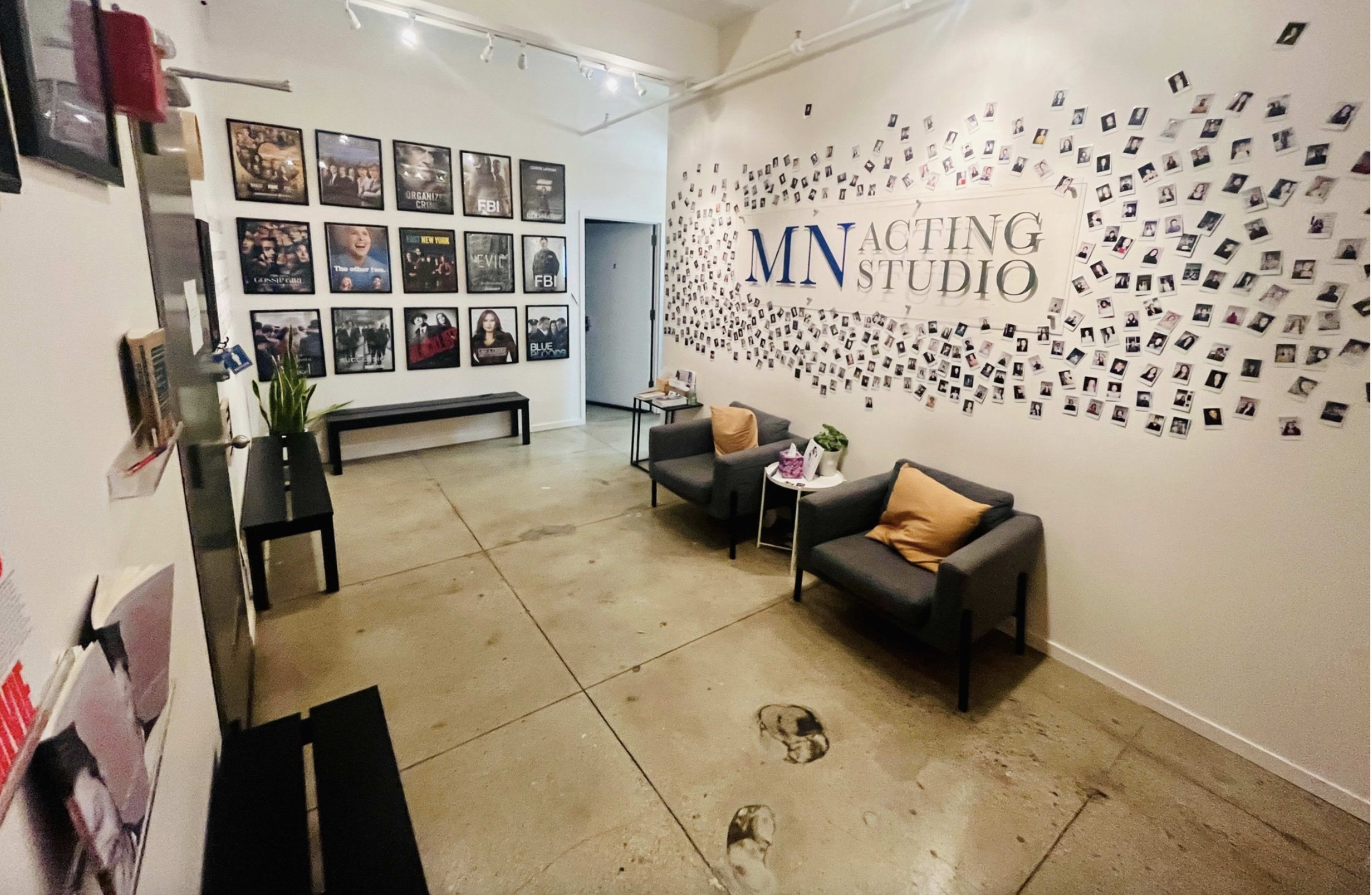 The image shows the interior of an acting studio featuring a waiting area with two armchairs, a long bench, a wall adorned with framed photos, and a large sign reading "MN ACTING STUDIO."
