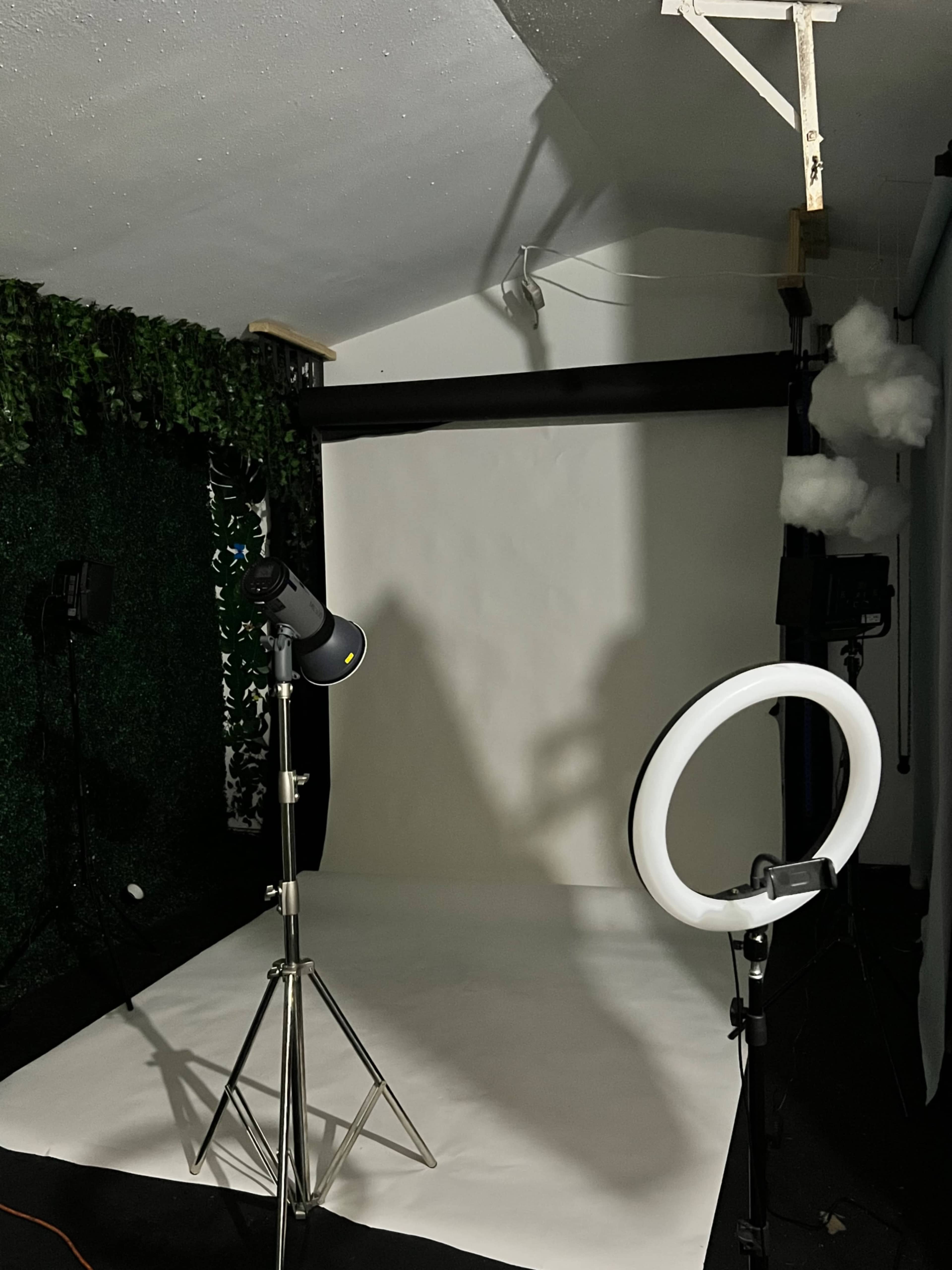 A photography studio setup with a white backdrop, a ring light, and various lighting equipment.