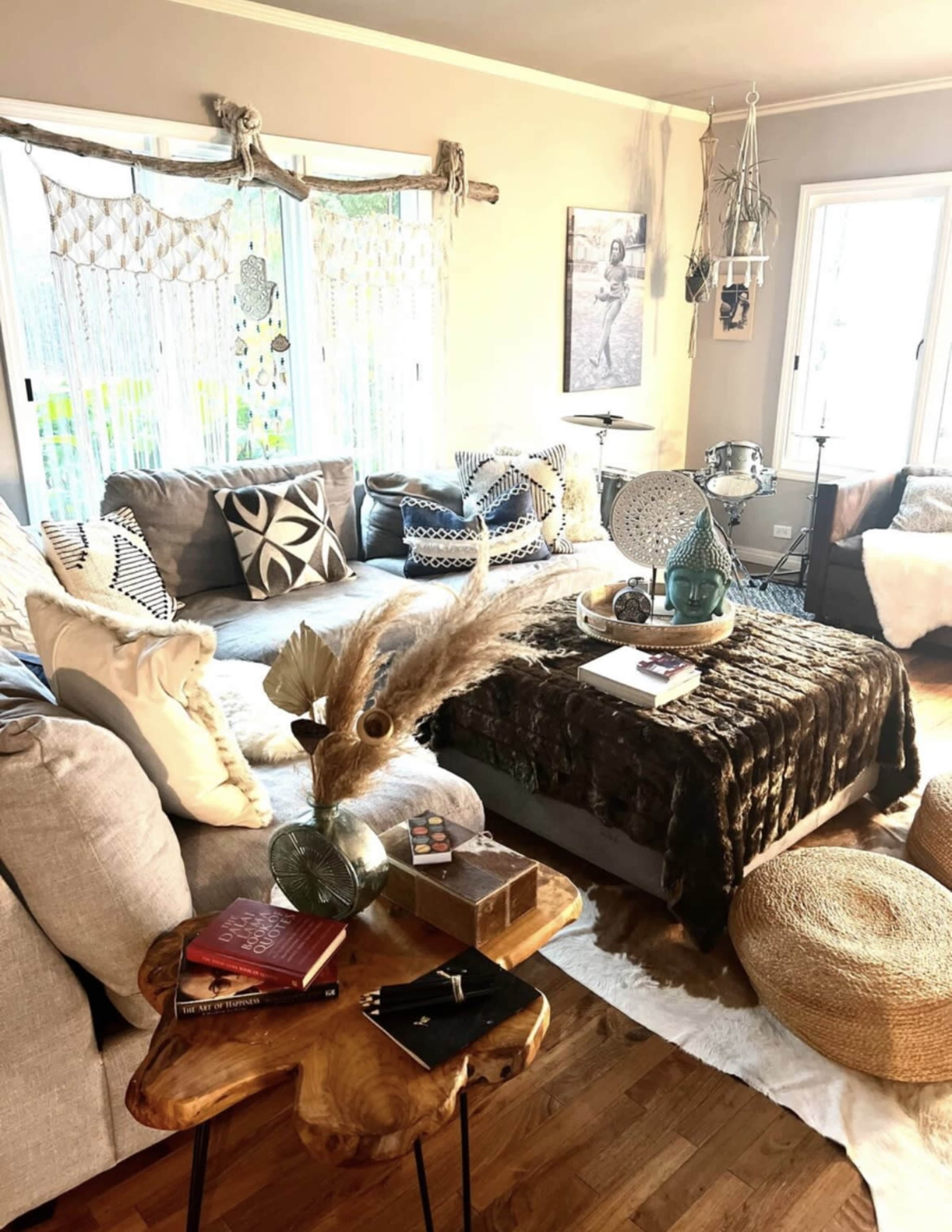The image shows a cozy living room with a large sectional sofa, a wooden coffee table, and decorative items including pillows, a woven throw, and a floor pouf.