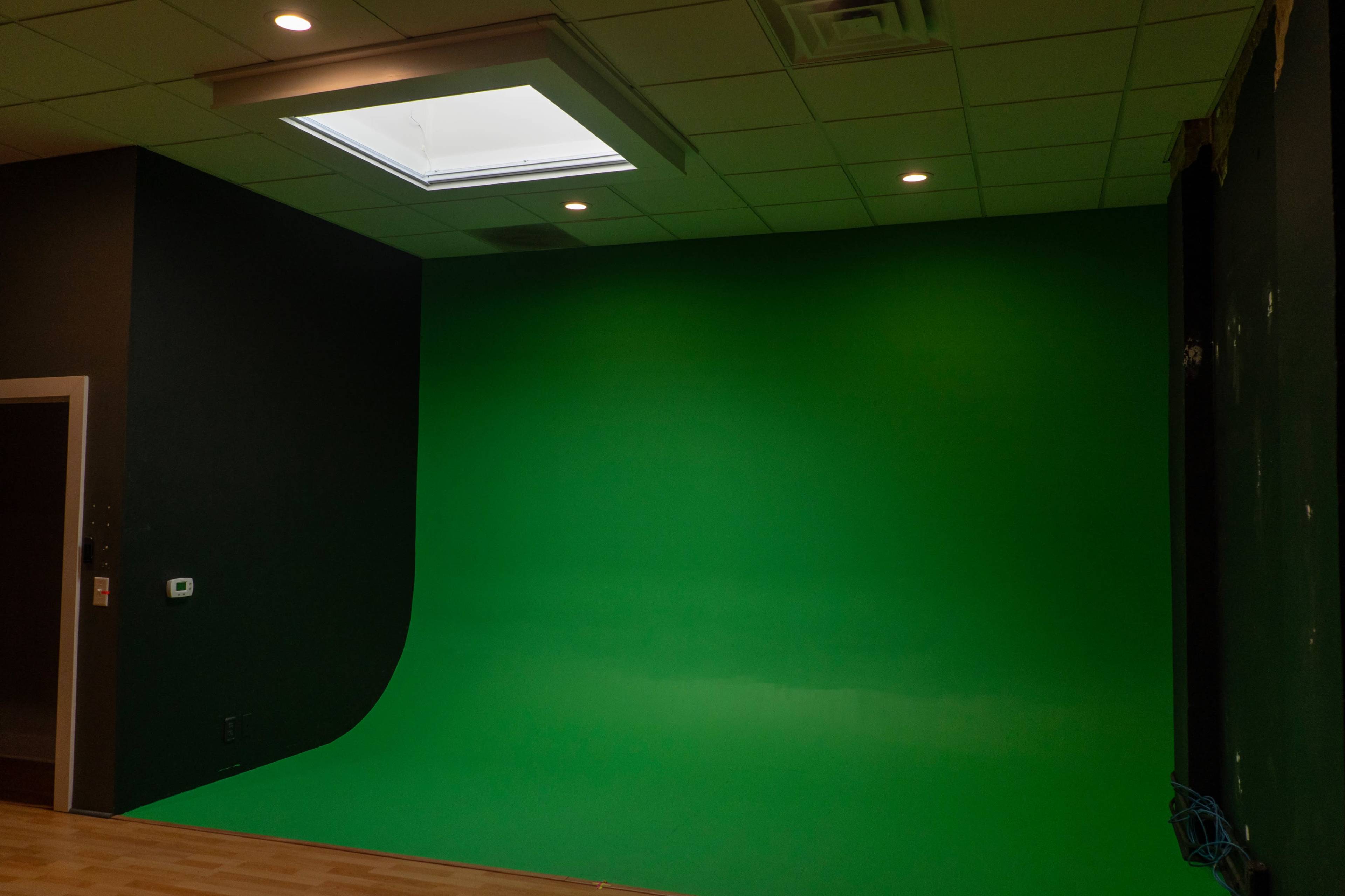 A room with a curved green screen setup against a dark wall and a skylight above.