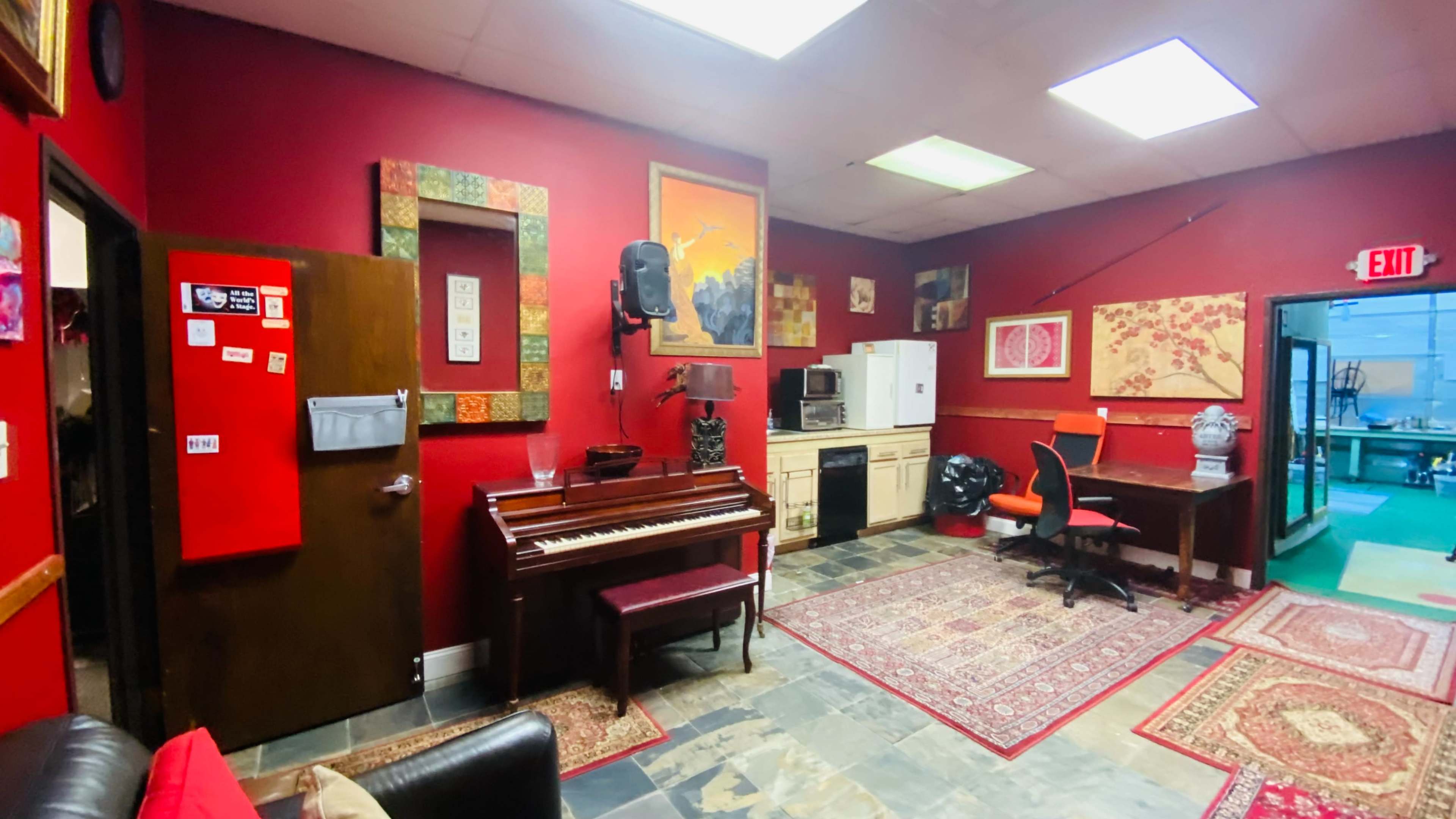The room features a red-walled interior with a piano, a refrigerator, a desk, and various artworks hanging on the walls.