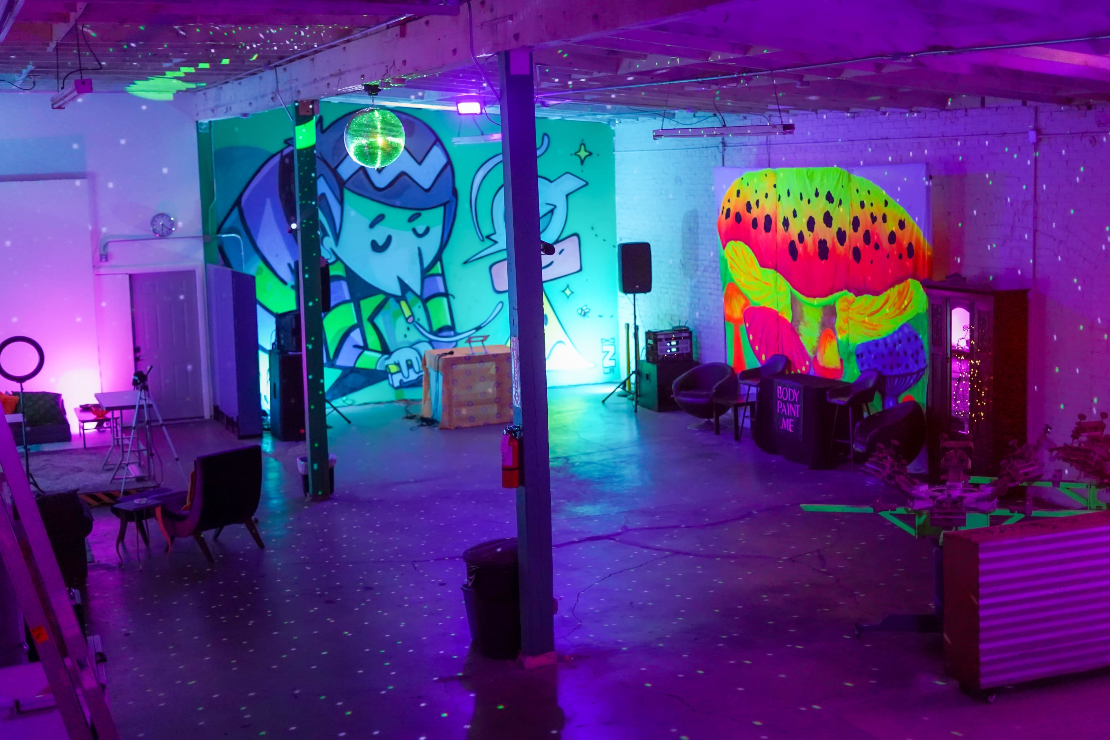 A vibrant, colorful event space features large graffiti murals, seating areas, and projected lights creating a dynamic atmosphere.