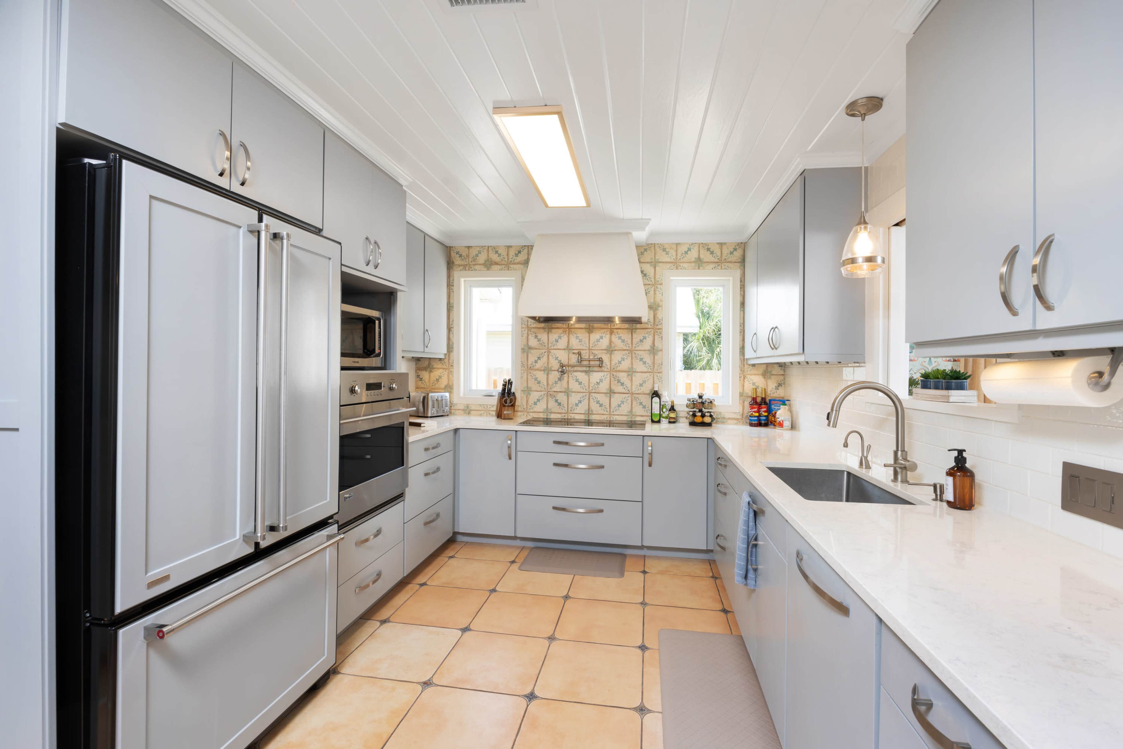 The kitchen features gray cabinetry, stainless steel appliances, a white marble countertop, and a decorative tile backsplash.