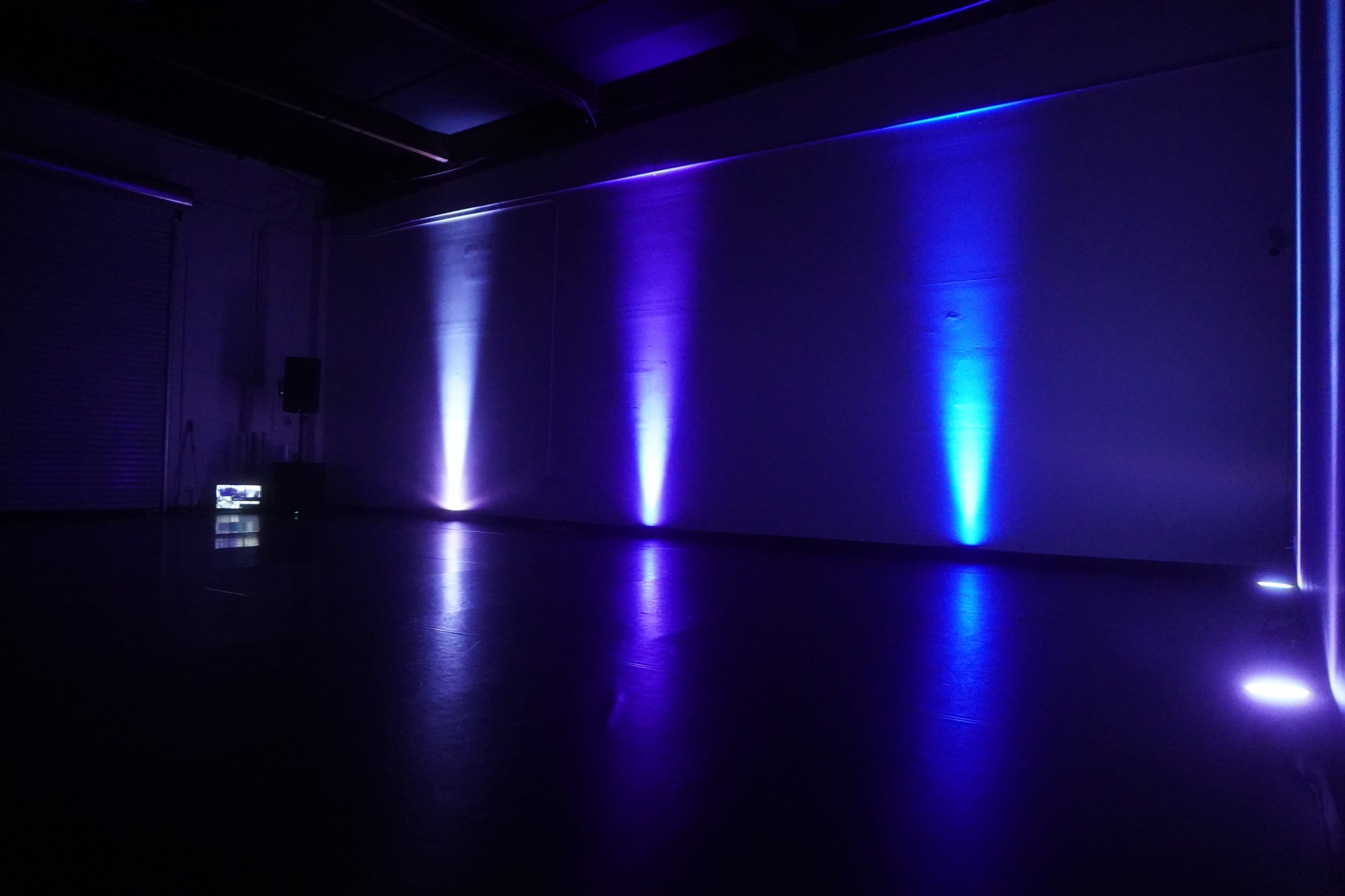 A dimly lit room with purple and blue lights illuminating the walls and a speaker placed on the floor.