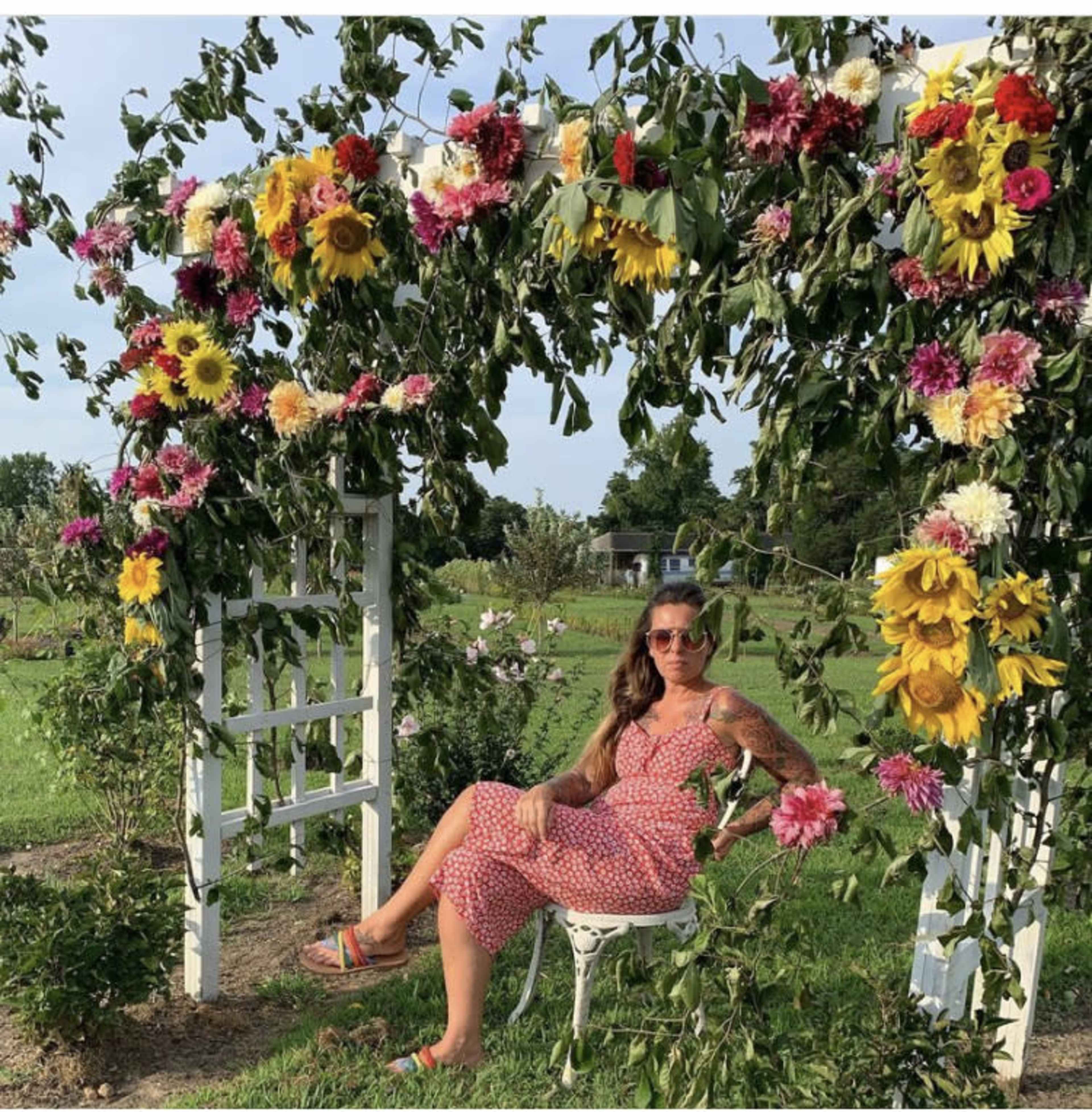 A person sits on a chair under an archway adorned with various flowers in a garden setting.