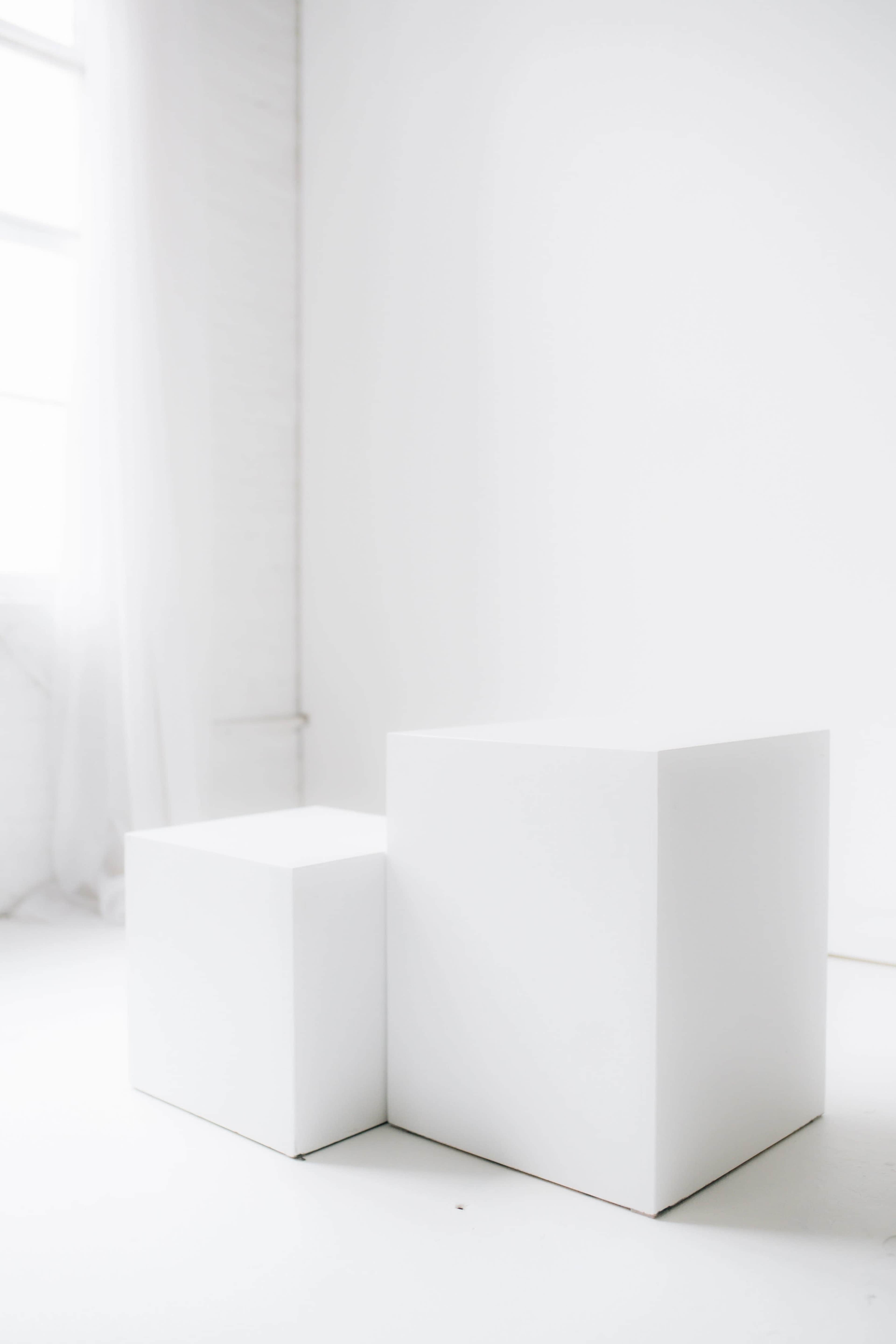 Two white geometric cubes are placed on a white floor in a bright, minimally decorated room.