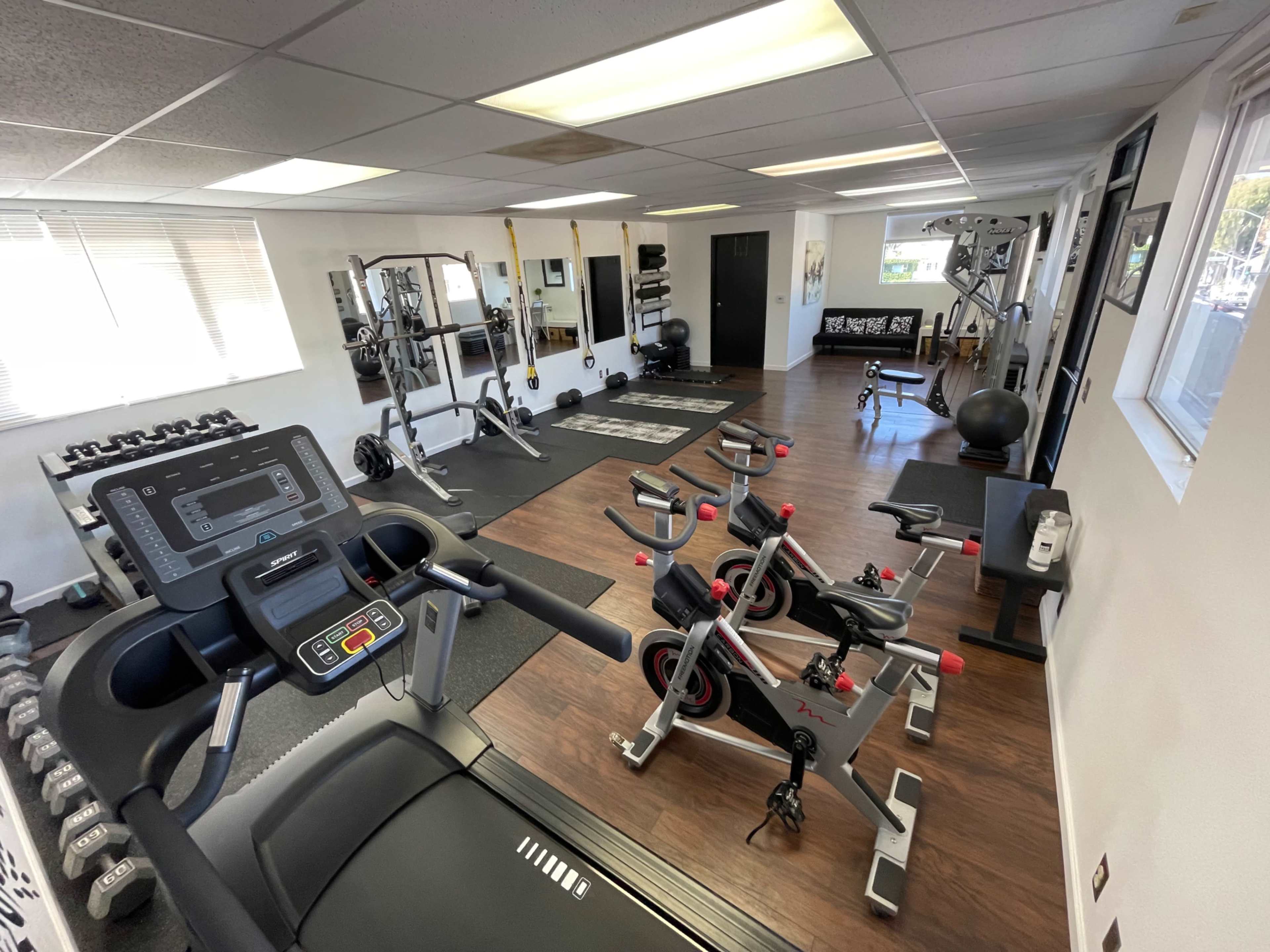 The image shows a well-equipped gym with various exercise machines, free weights, and workout mats arranged neatly in a spacious area.