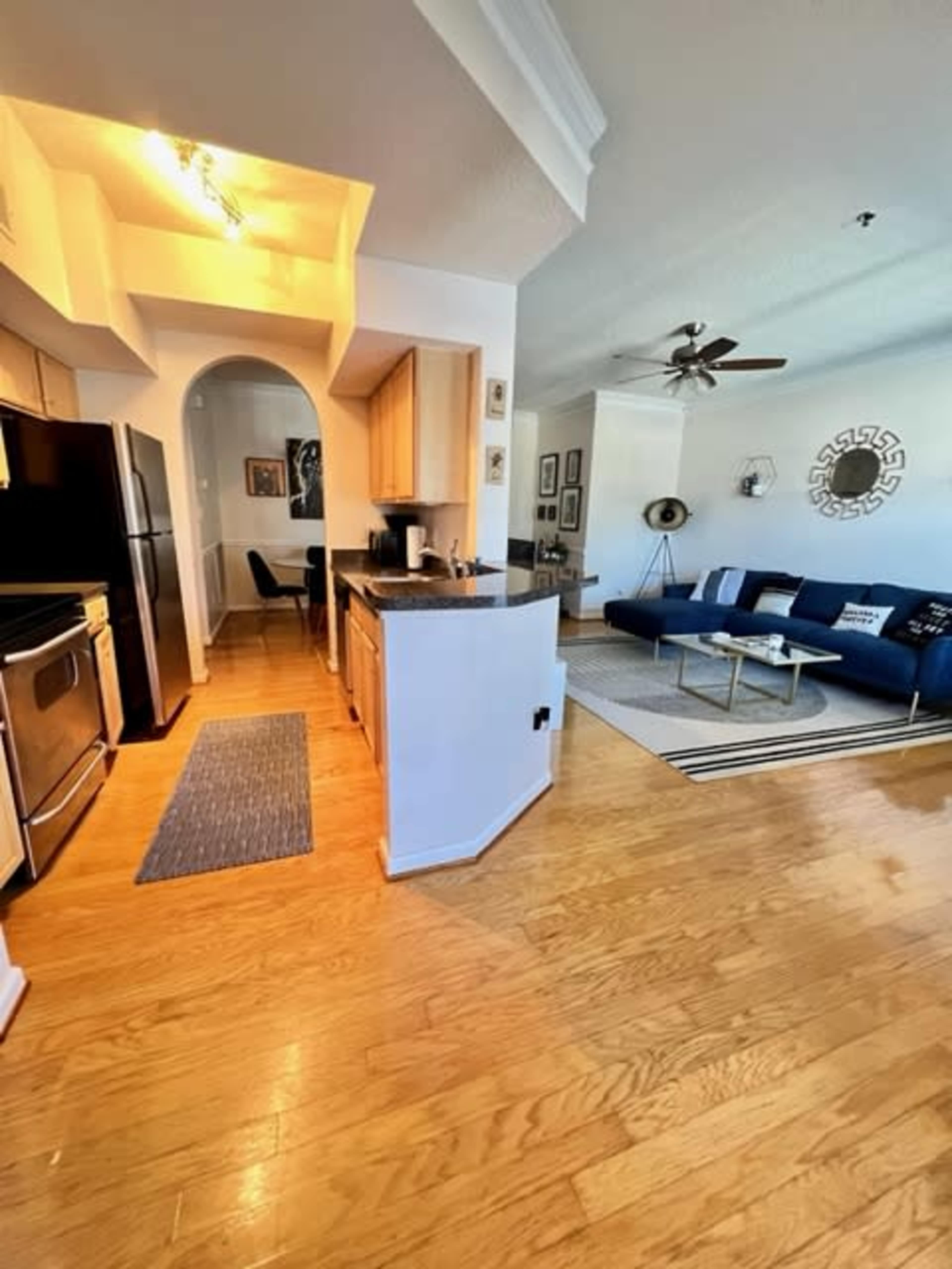 A spacious kitchen area leading into a living room with wooden flooring, stainless steel appliances, and a blue sofa.