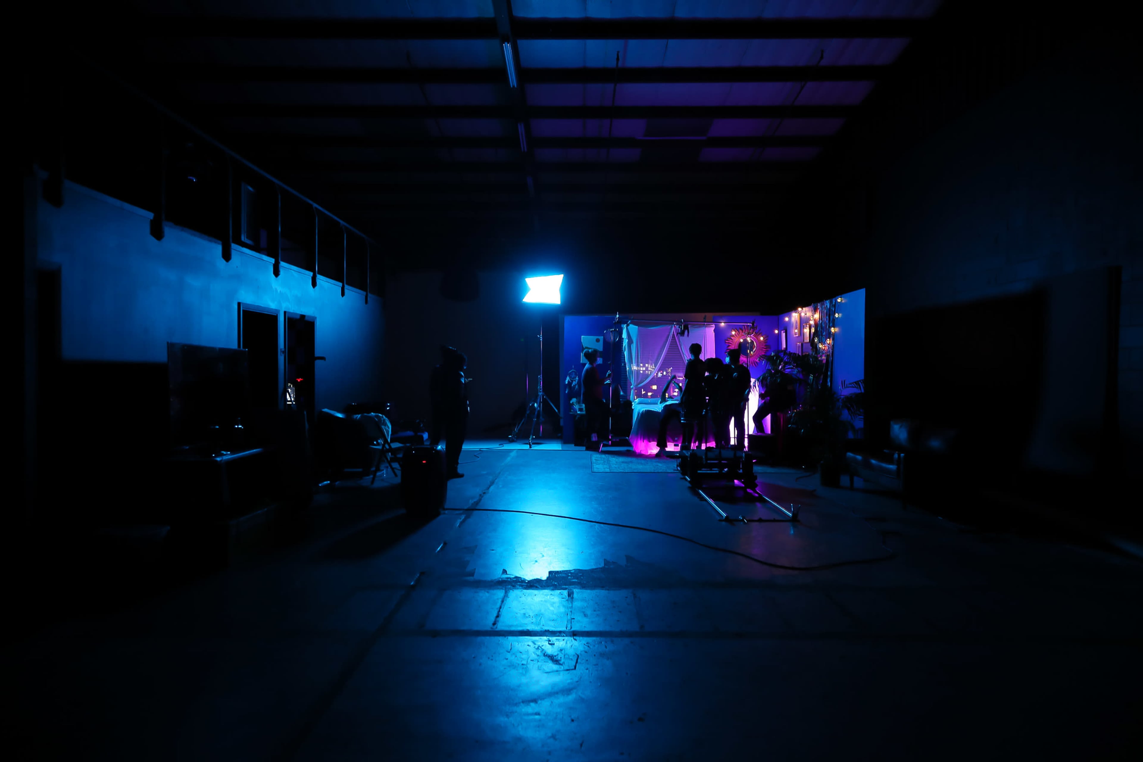 A dimly lit studio space features silhouettes of people working near colorful lighting equipment.