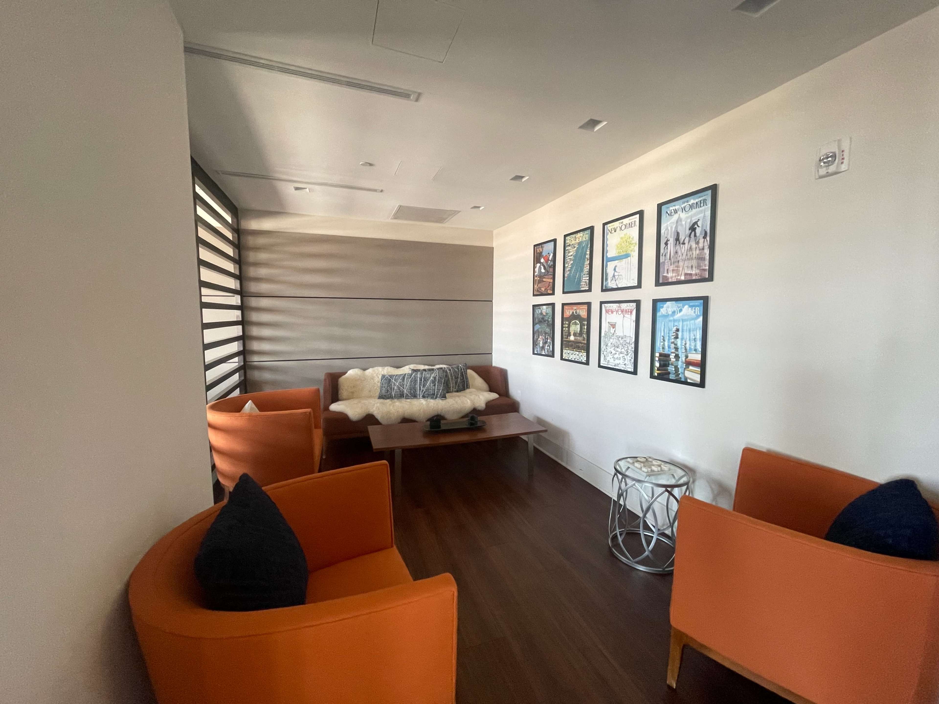 A small lounge area with two orange chairs, a couch, a coffee table, and framed posters on the wall.