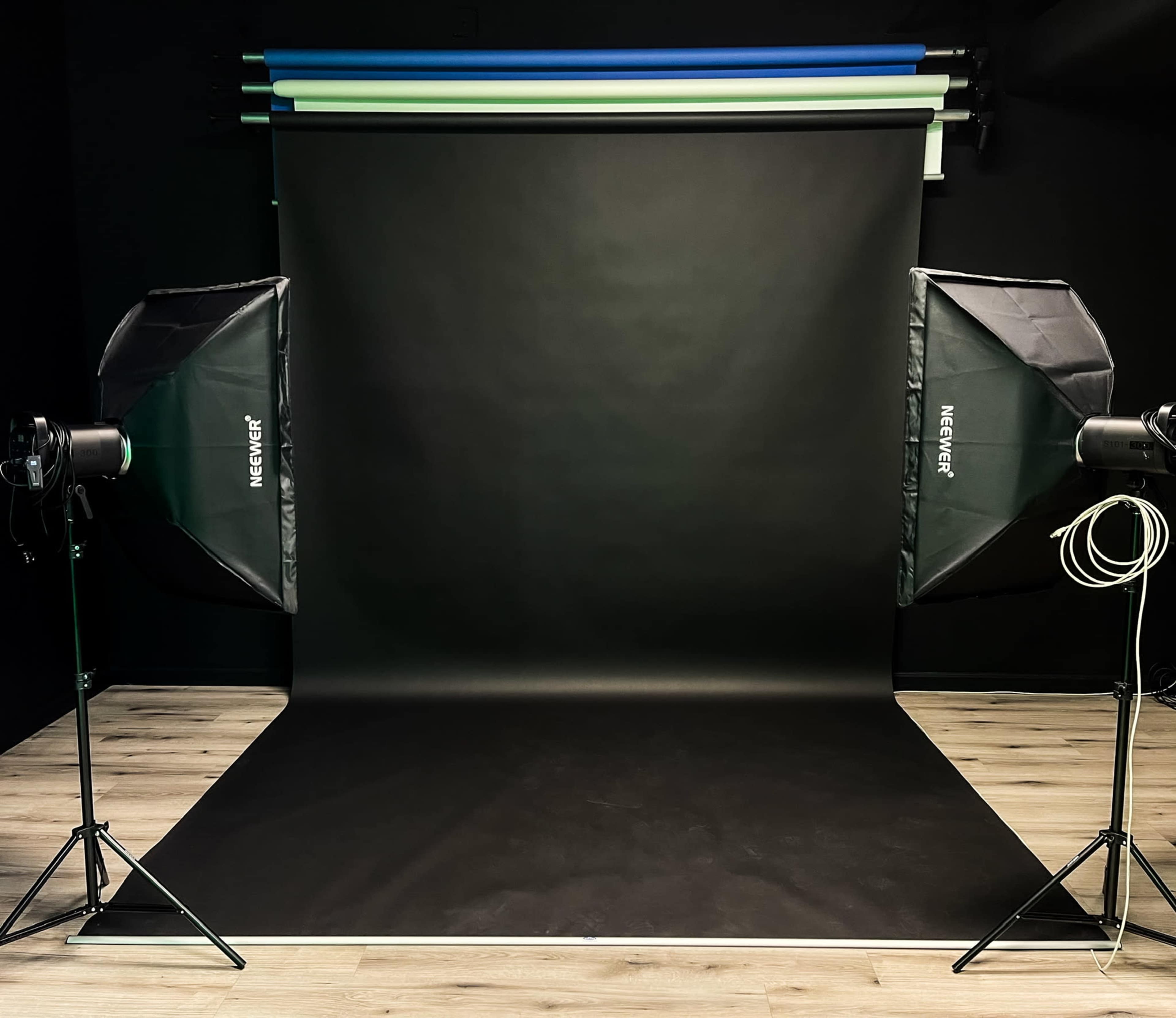 A photography studio with a black backdrop and two lighting softboxes on stands.
