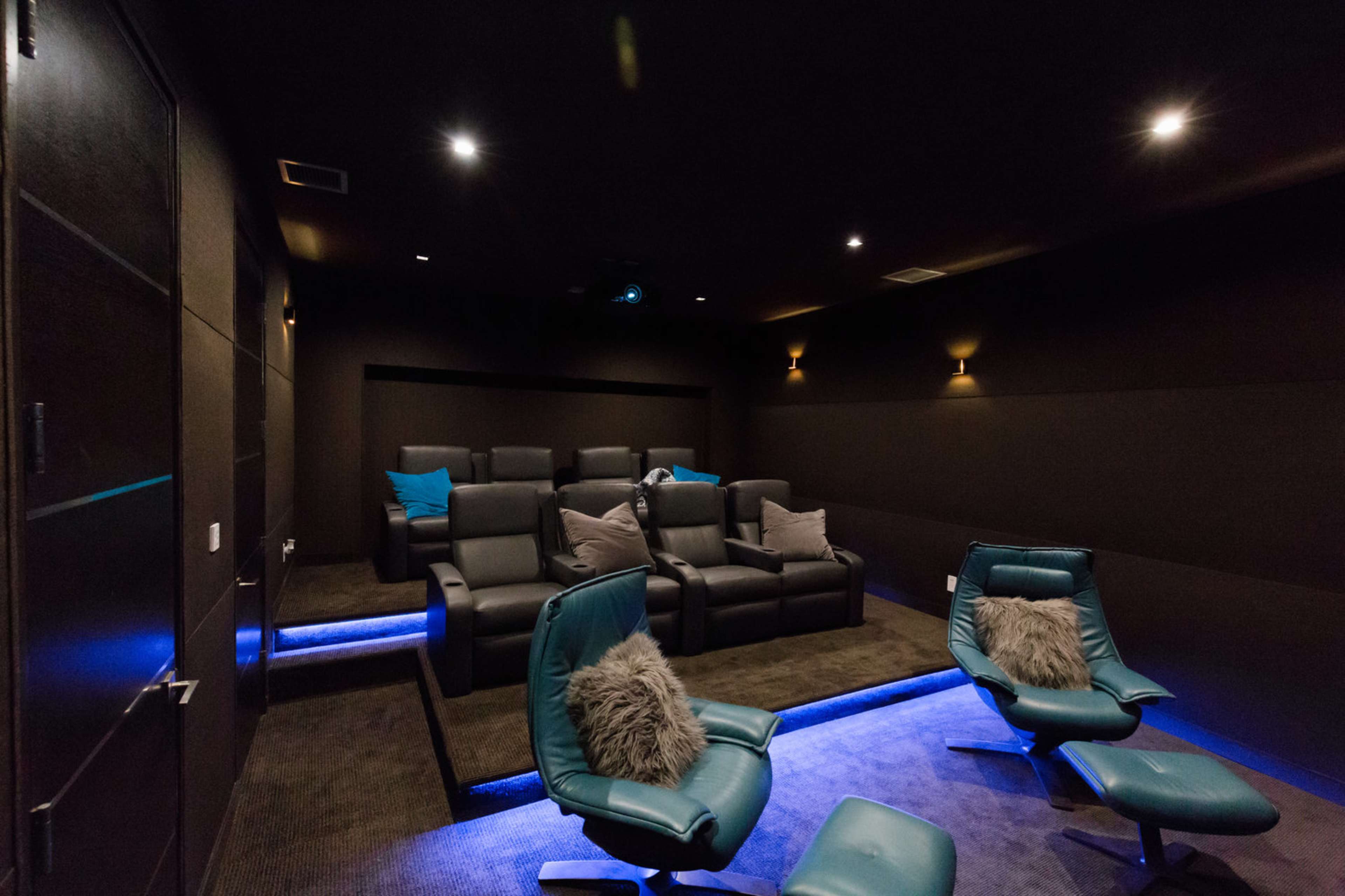 A modern home theater with tiered seating, blue accent lighting, and dark walls.