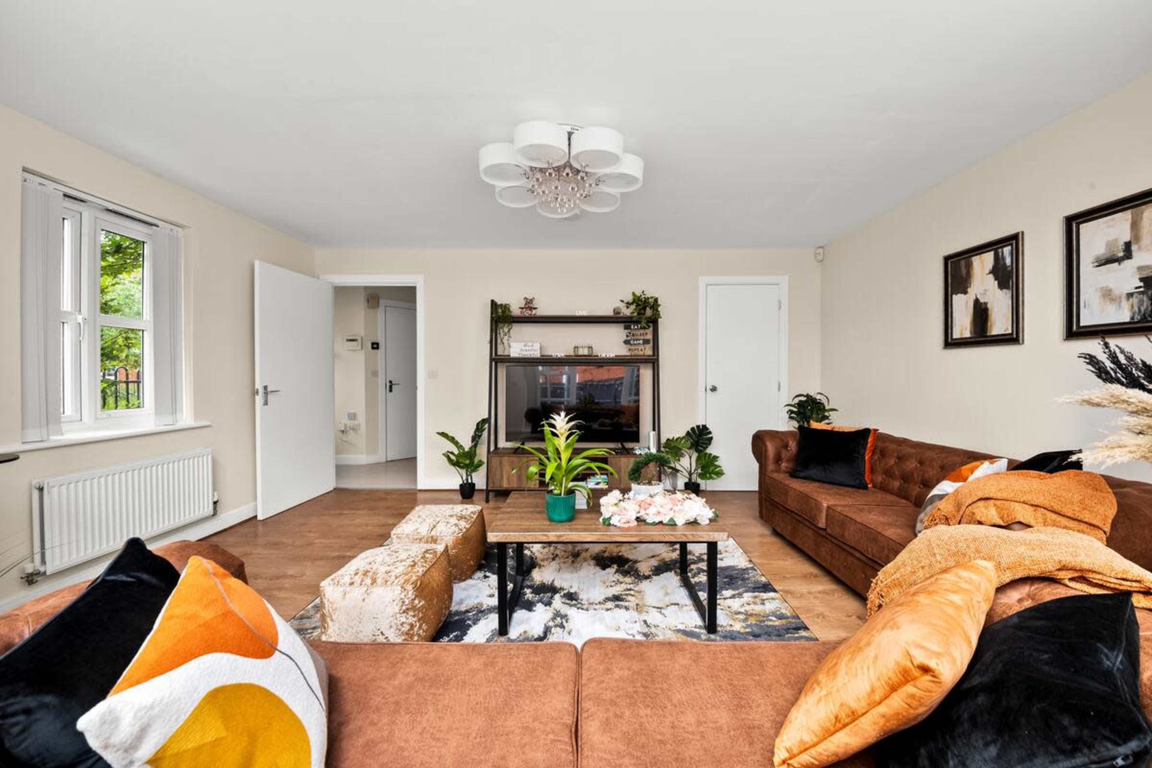 The living room features two brown sofas, a coffee table with decorative items, a television on a stand, and light-colored walls with framed artwork.